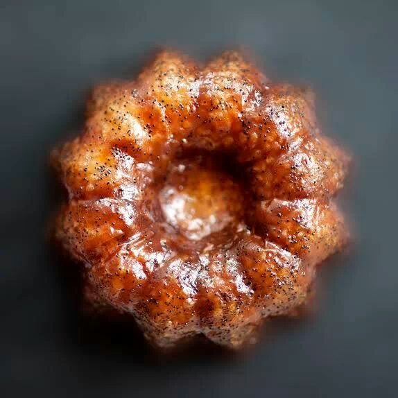 A close-up of a small, round, caramelized cannele pastry with a shiny glaze on top.