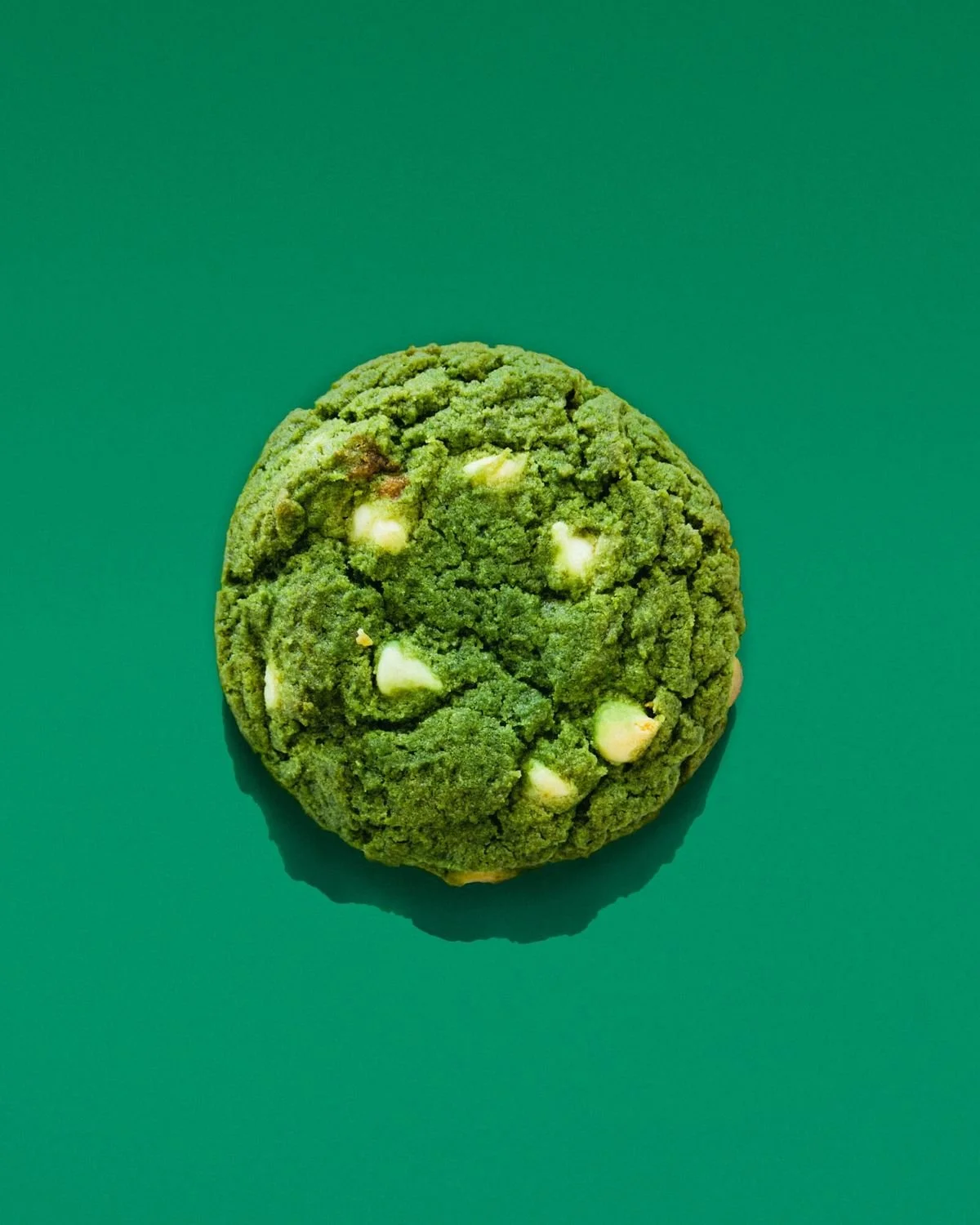 A green matcha cookie with white chocolate chips on a green background.