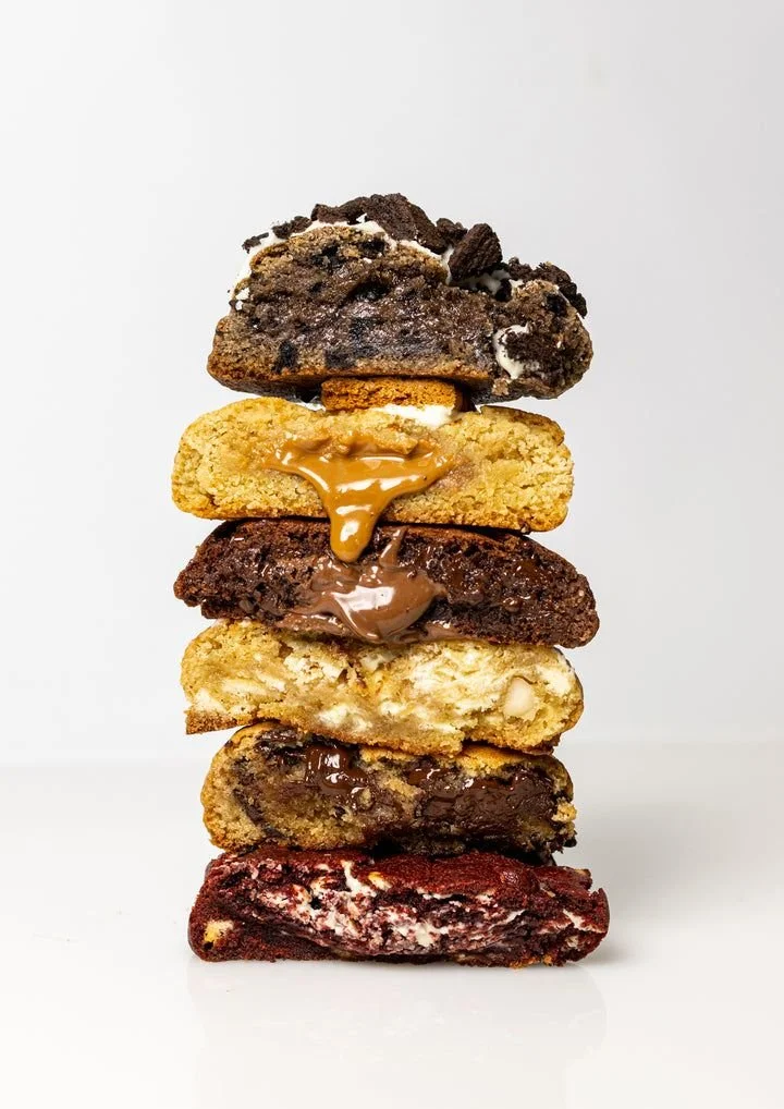 Stack of six assorted cookies with various flavors and toppings, against a plain white background.