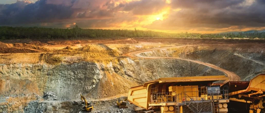 Paisaje de un yacimiento minero con maquinaria pesada y una carretera en un terreno excavado, al atardecer.