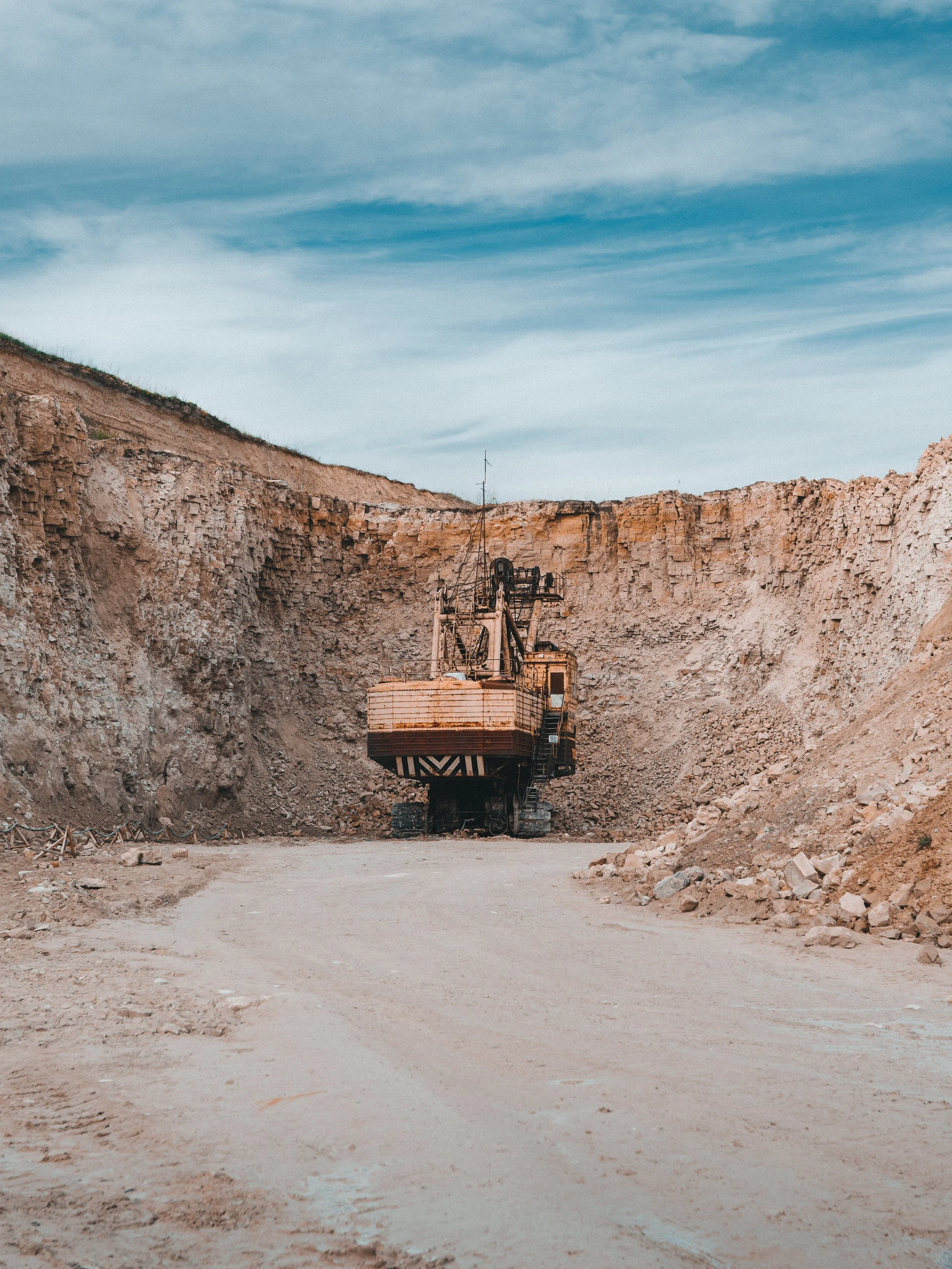 Excavadora en un sitio de construcción o minería, rodeada de tierra y rocas, con cielo despejado en el fondo.