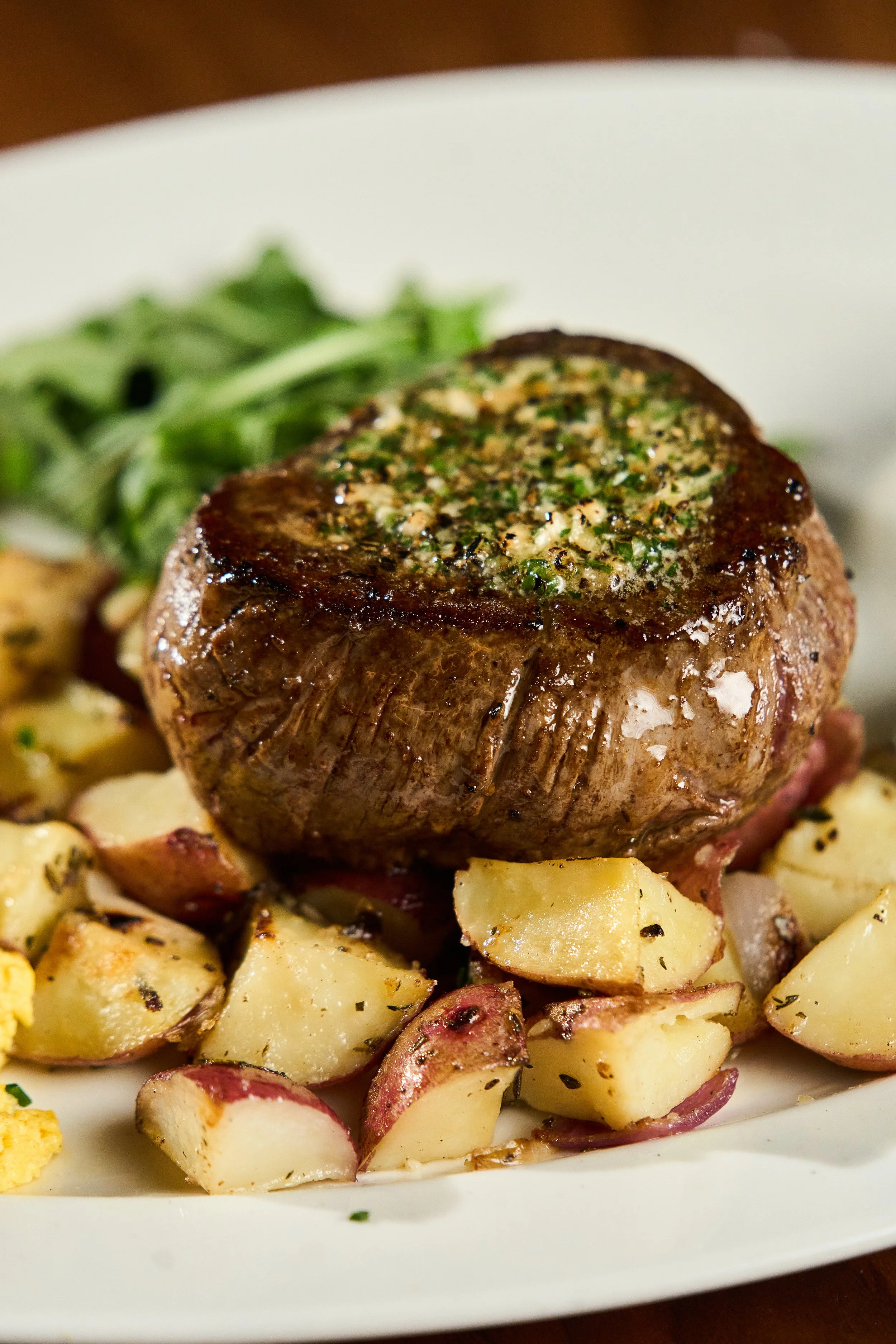 A plate with a cooked steak topped with herb butter, accompanied by roasted potatoes and a side of green salad.