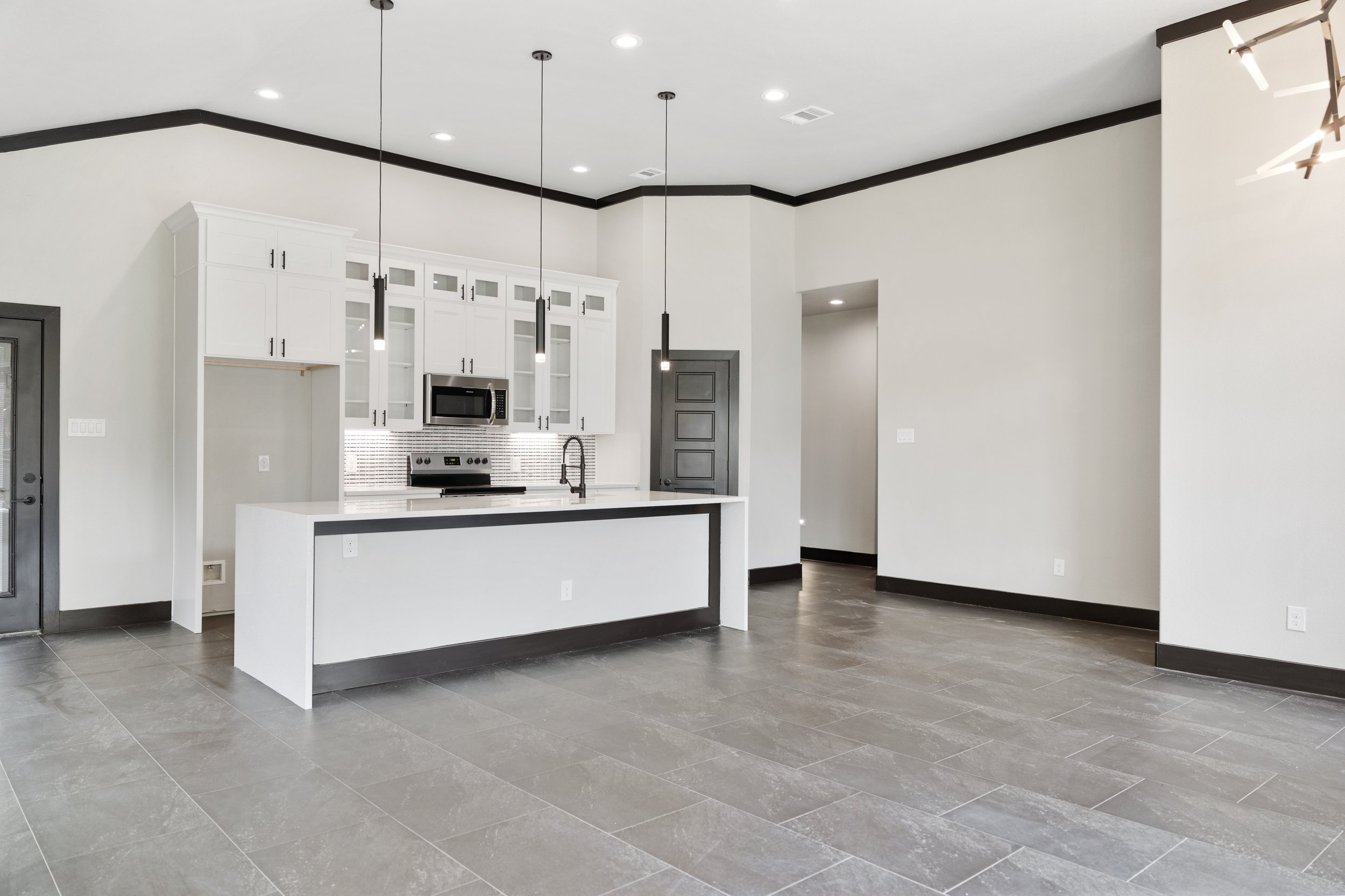 Modern, empty kitchen and living area with white cabinets, gray trim, and gray tile floors.