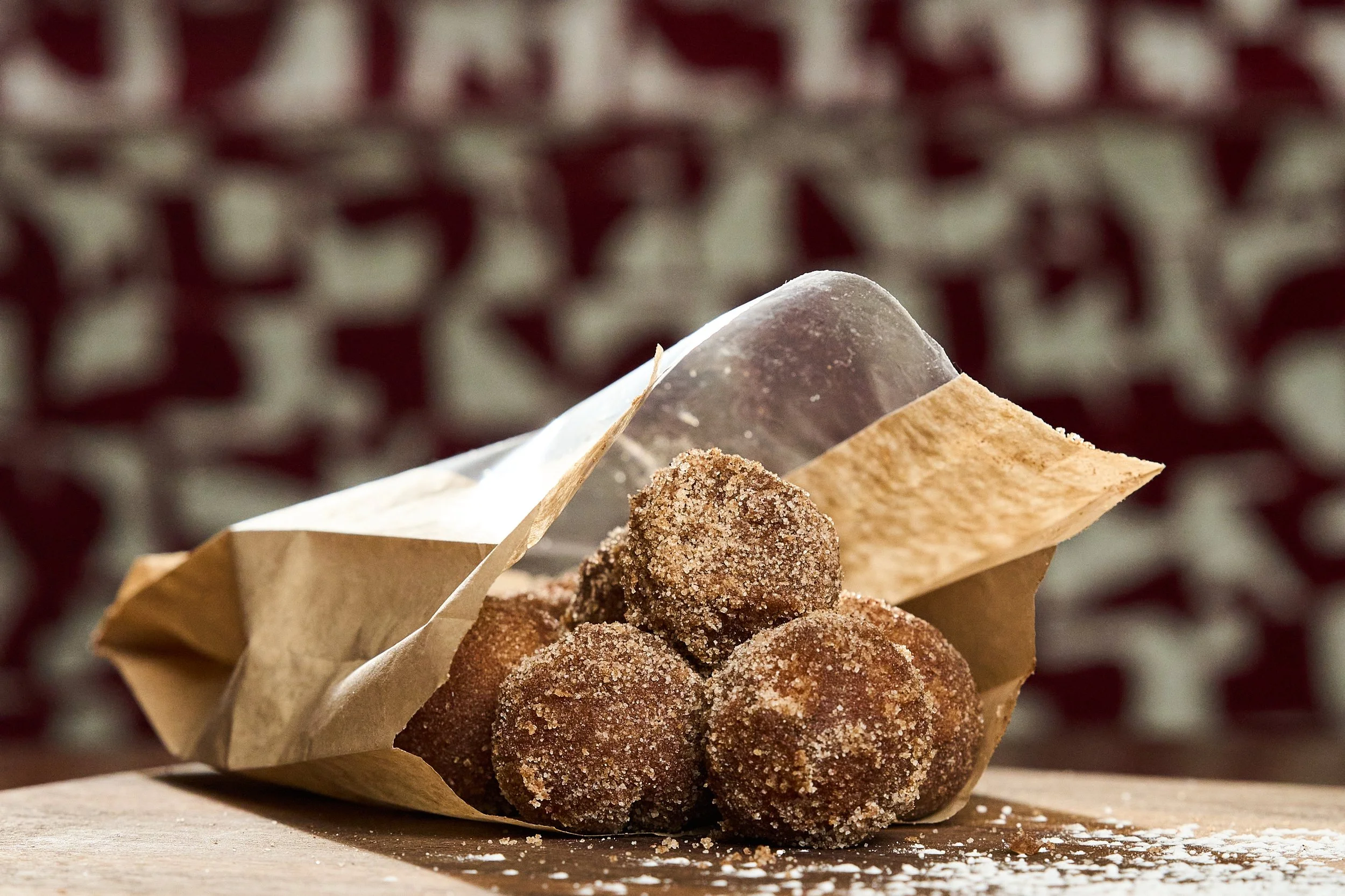 Fried sugar-coated doughnut holes wrapped in parchment paper on a wooden surface.