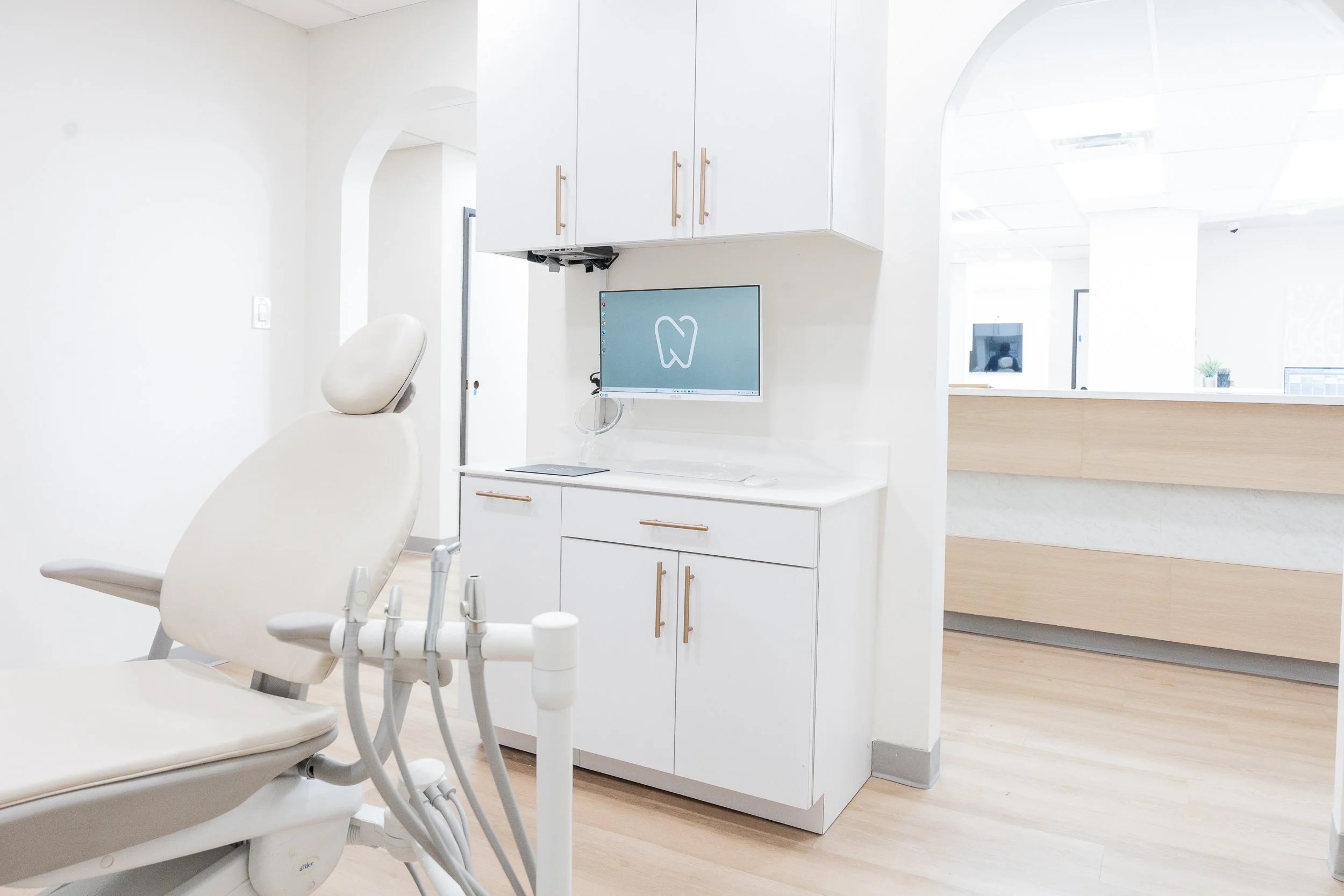 Dental examination room with a dental chair, monitor, and cabinetry in a modern clinic.