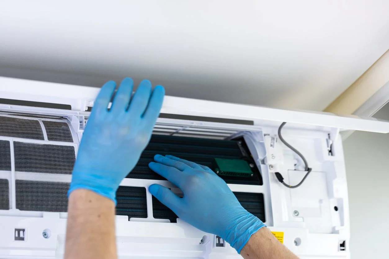 Person wearing blue gloves repairing the interior of an air conditioning unit.