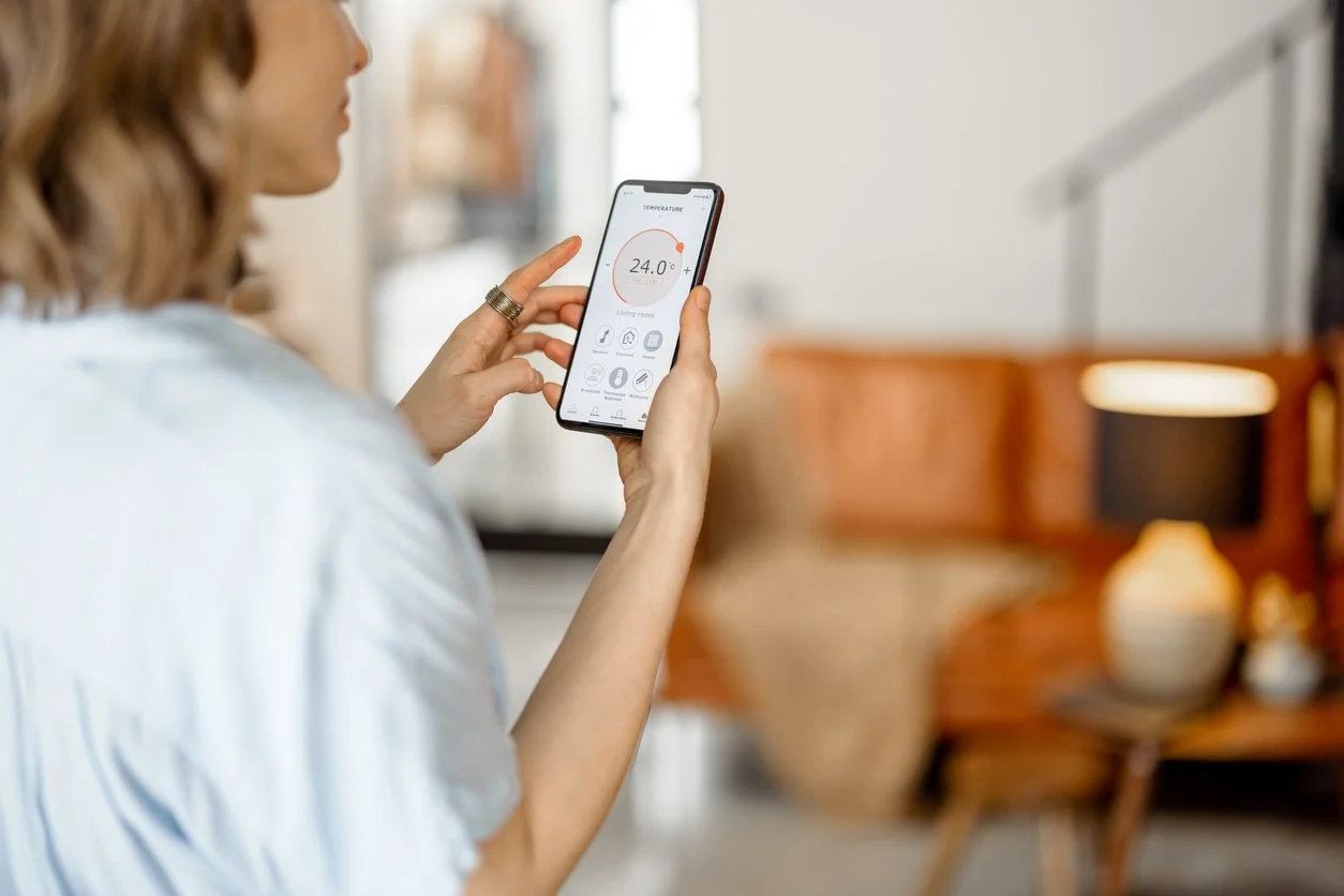 Woman adjusting a smart thermostat control on her smartphone in a living room.