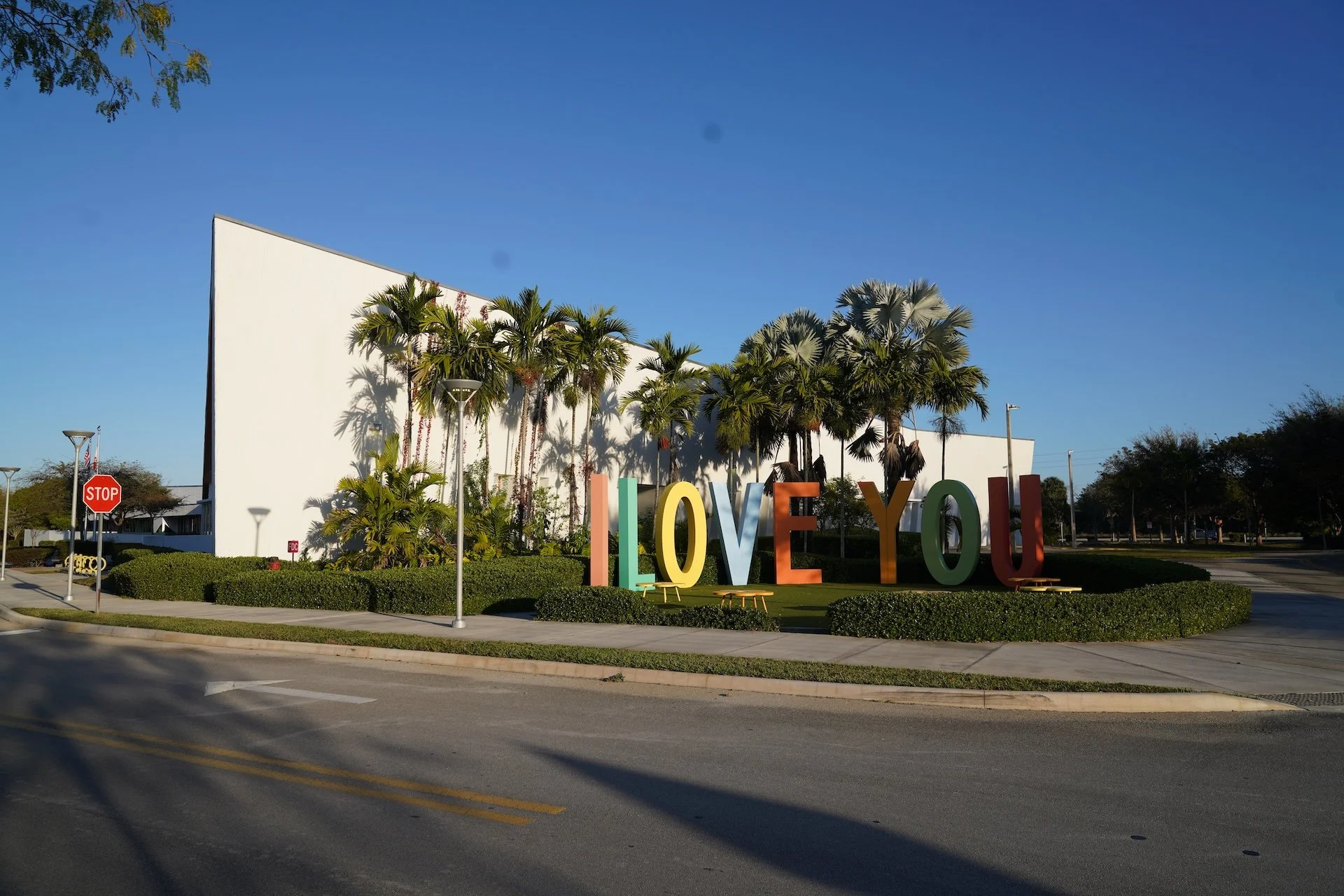 Large colorful letters spelling 'I LOVE YOU' in front of a white building with palm trees and a bright blue sky.
