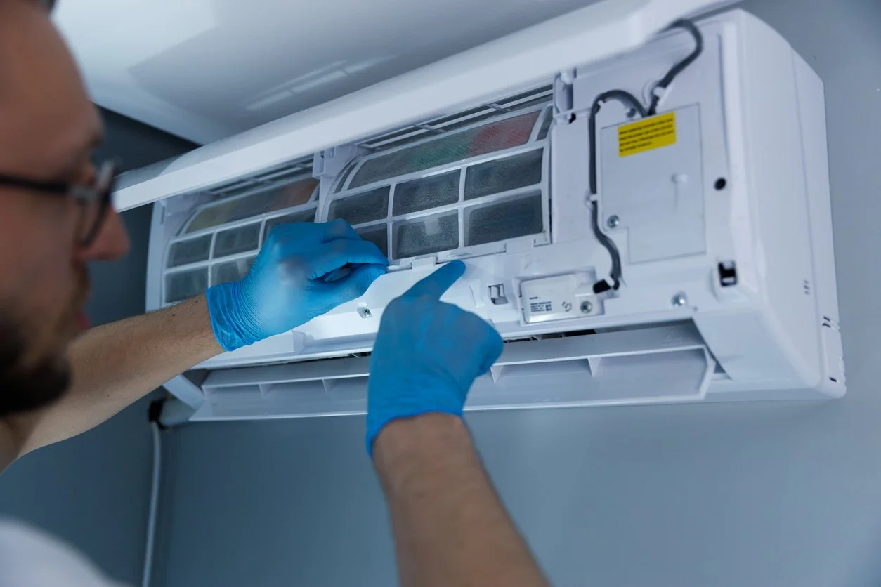 A technician in blue gloves repairing a wall-mounted air conditioning unit.
