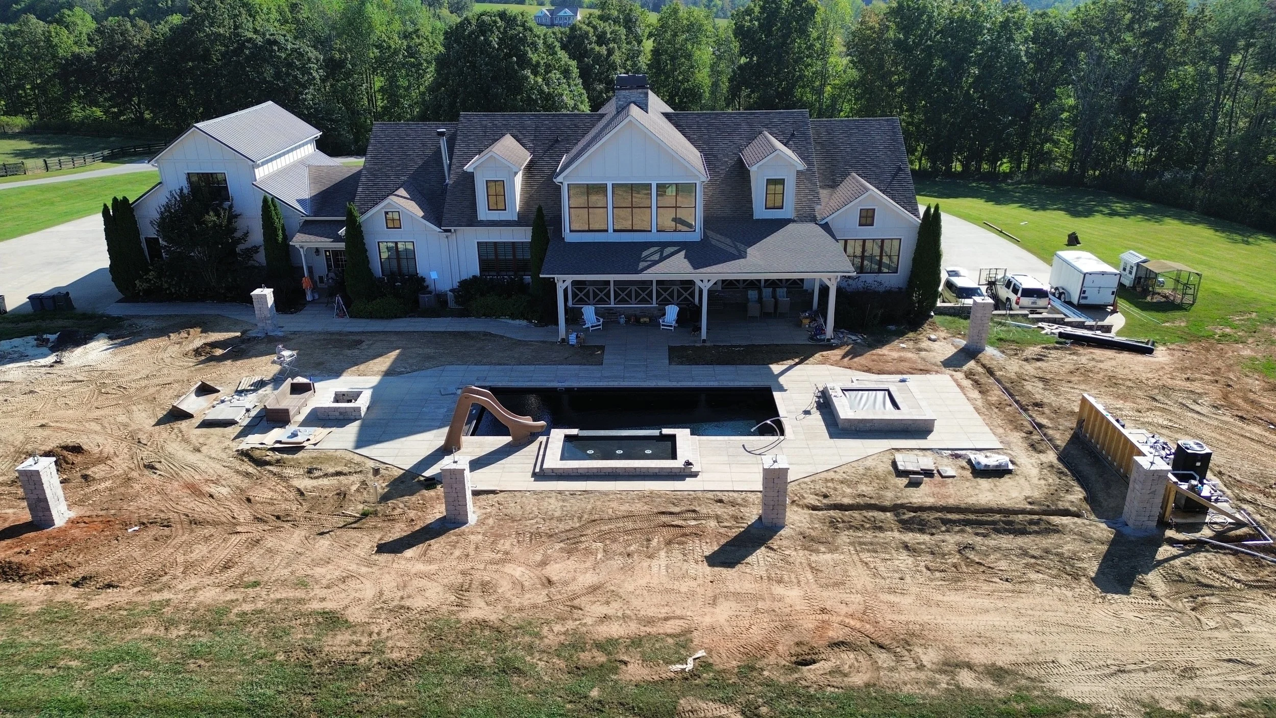 A large, two-story house under construction with a backyard pool and patio area, surrounded by a green lawn and trees.