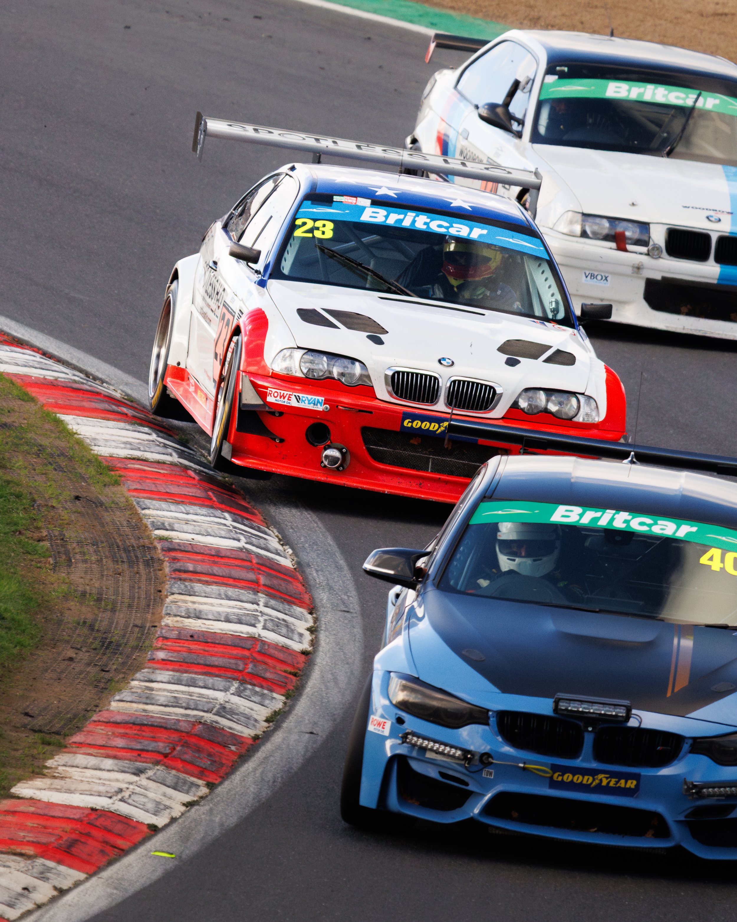 Race cars navigating a sharp turn on a race track, with a BMW in front and another race car behind, both marked with 'Britcar' sponsorship.