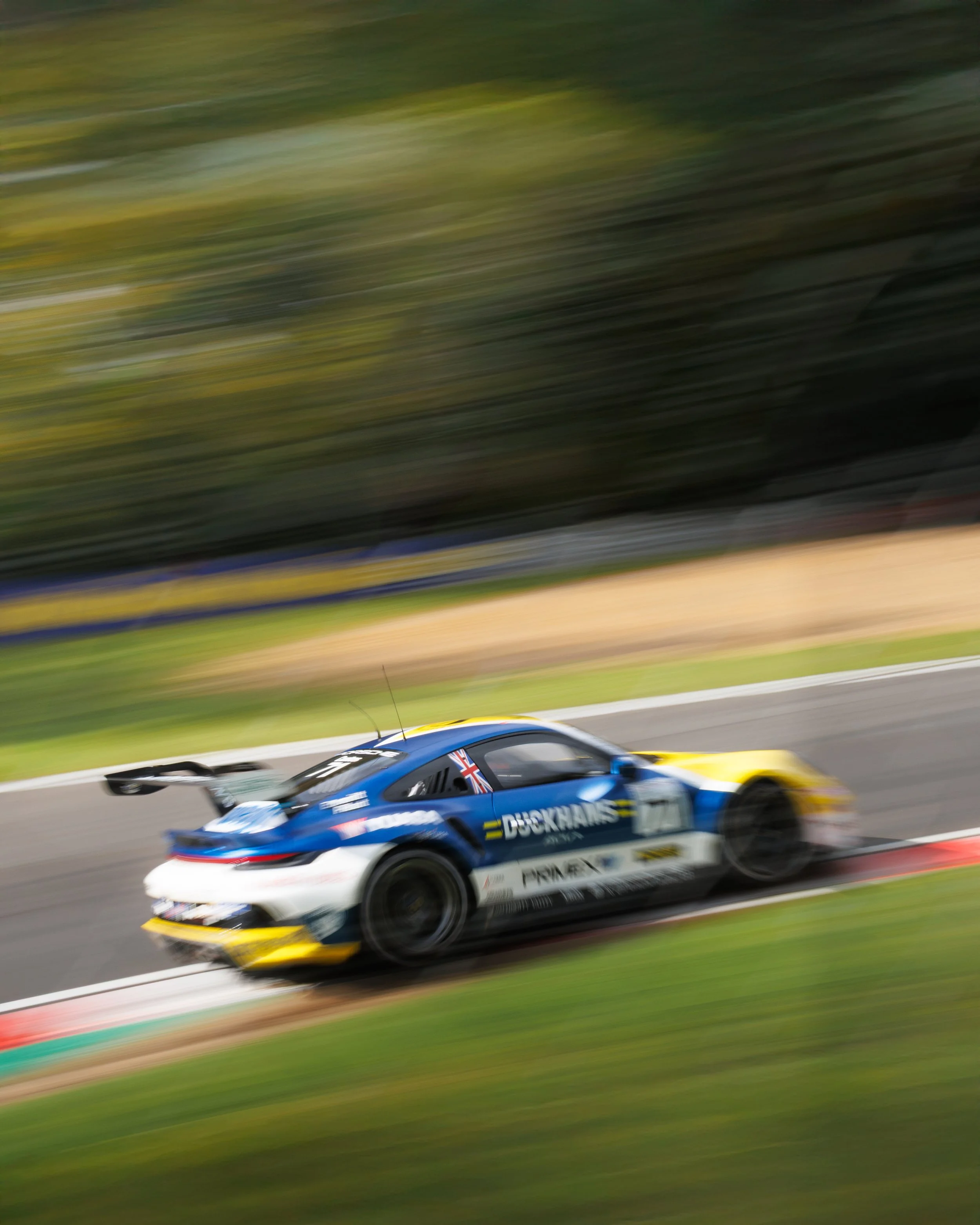 A blurred race car on a track, with a blue and yellow design and sponsorship logos, moving at high speed.