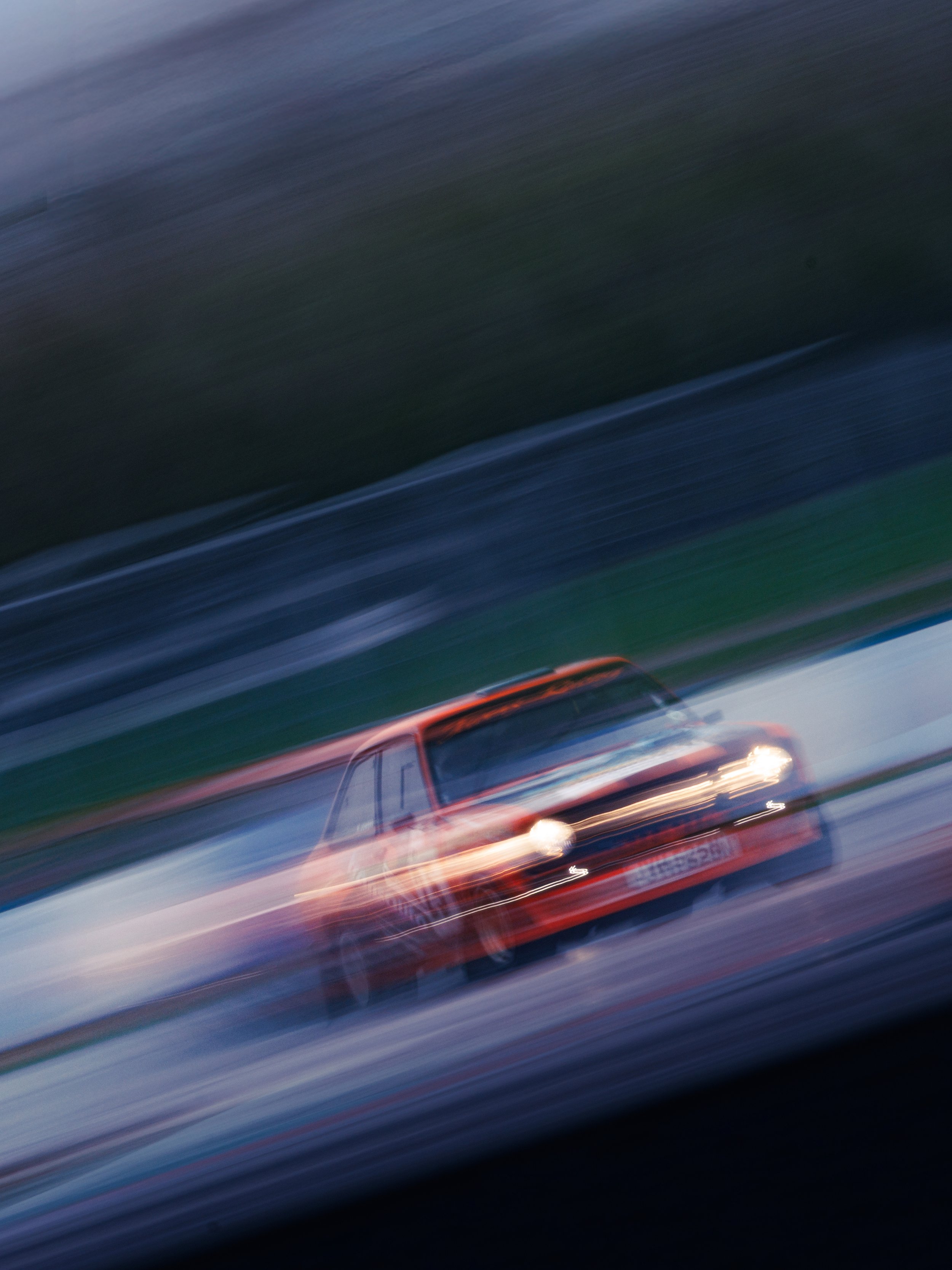 Moving photo of an orange race car on a track, with motion blur in the background and foreground.