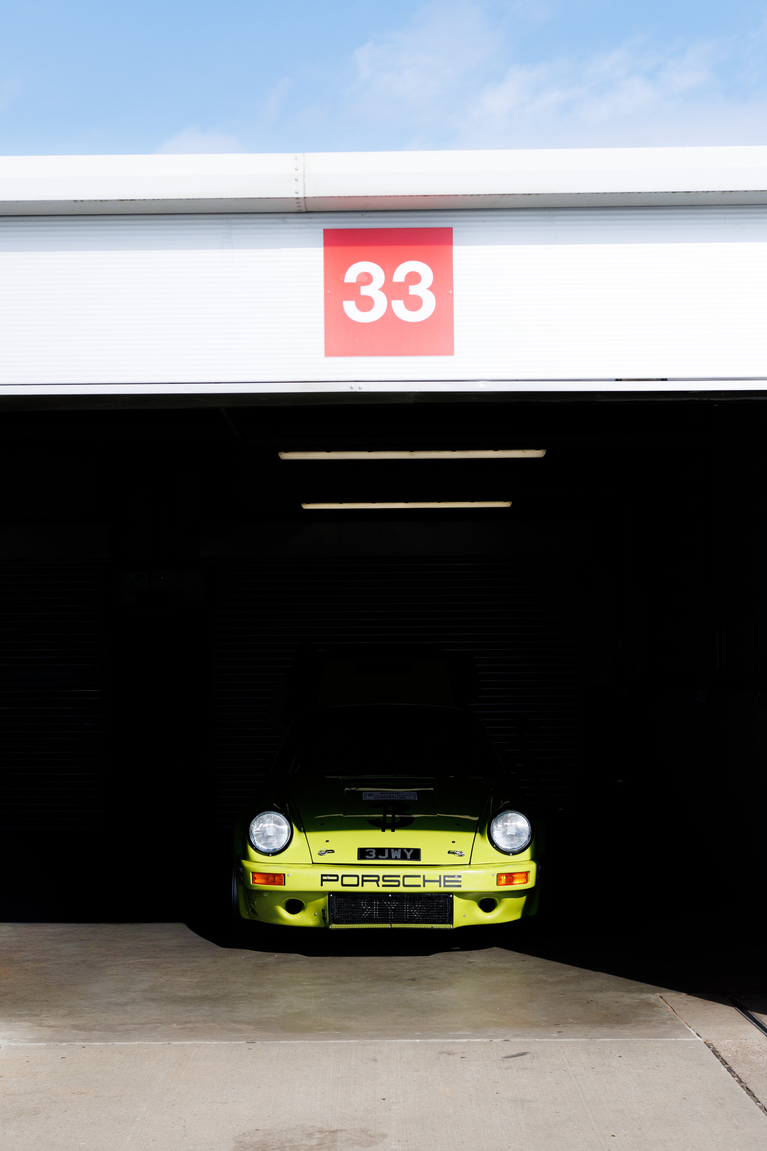 A green Porsche race car parked inside a garage with the number 33 sign above the entrance.