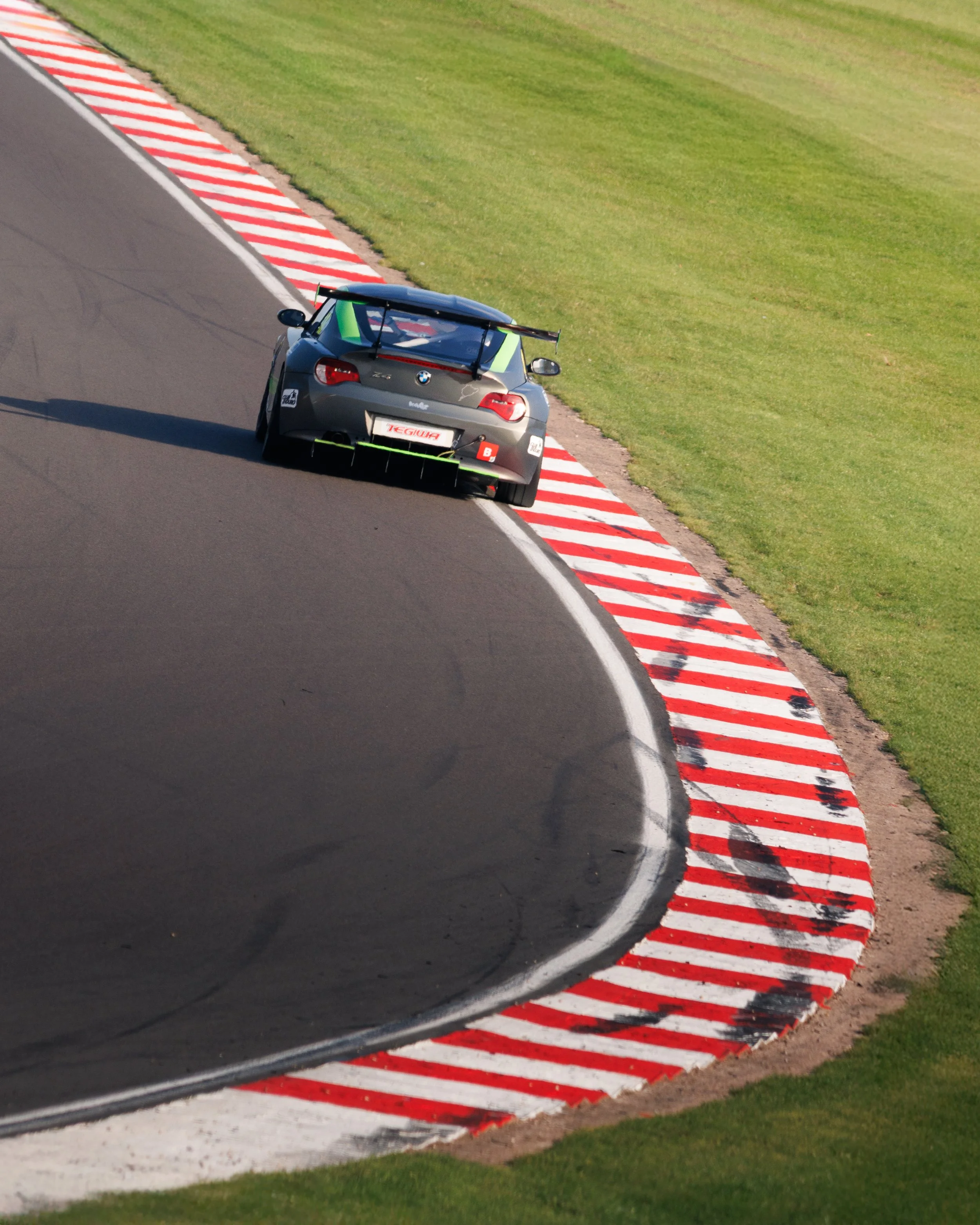 A race car driving on a curving race track with green grass on the sides.