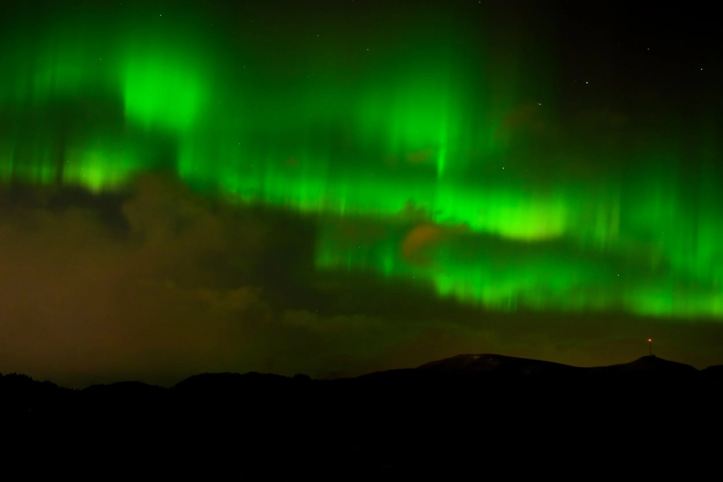 Northern lights or aurora borealis in the night sky over a dark landscape.