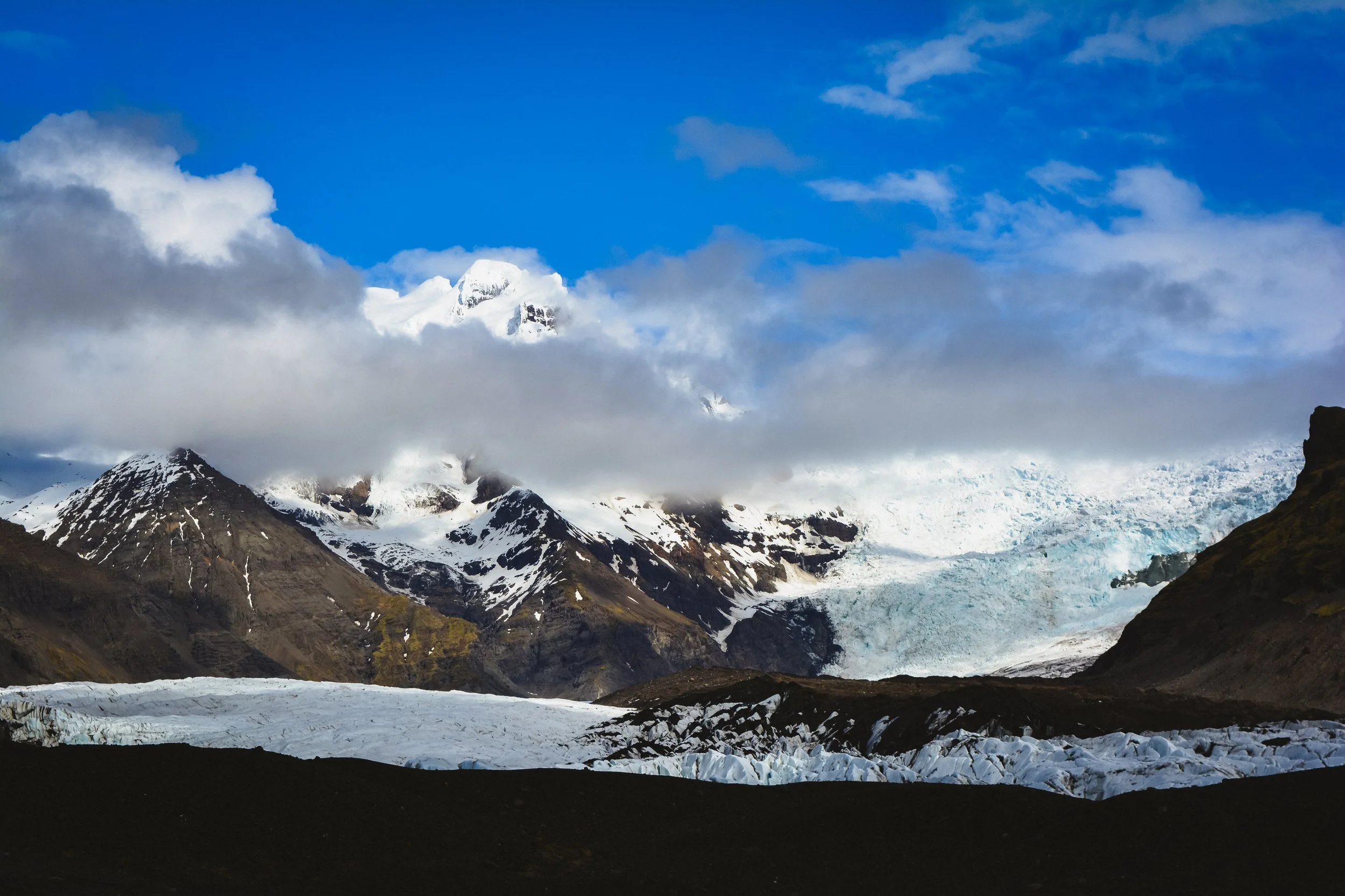 Snow-capped mountains and glaciers under a partly cloudy blue sky.