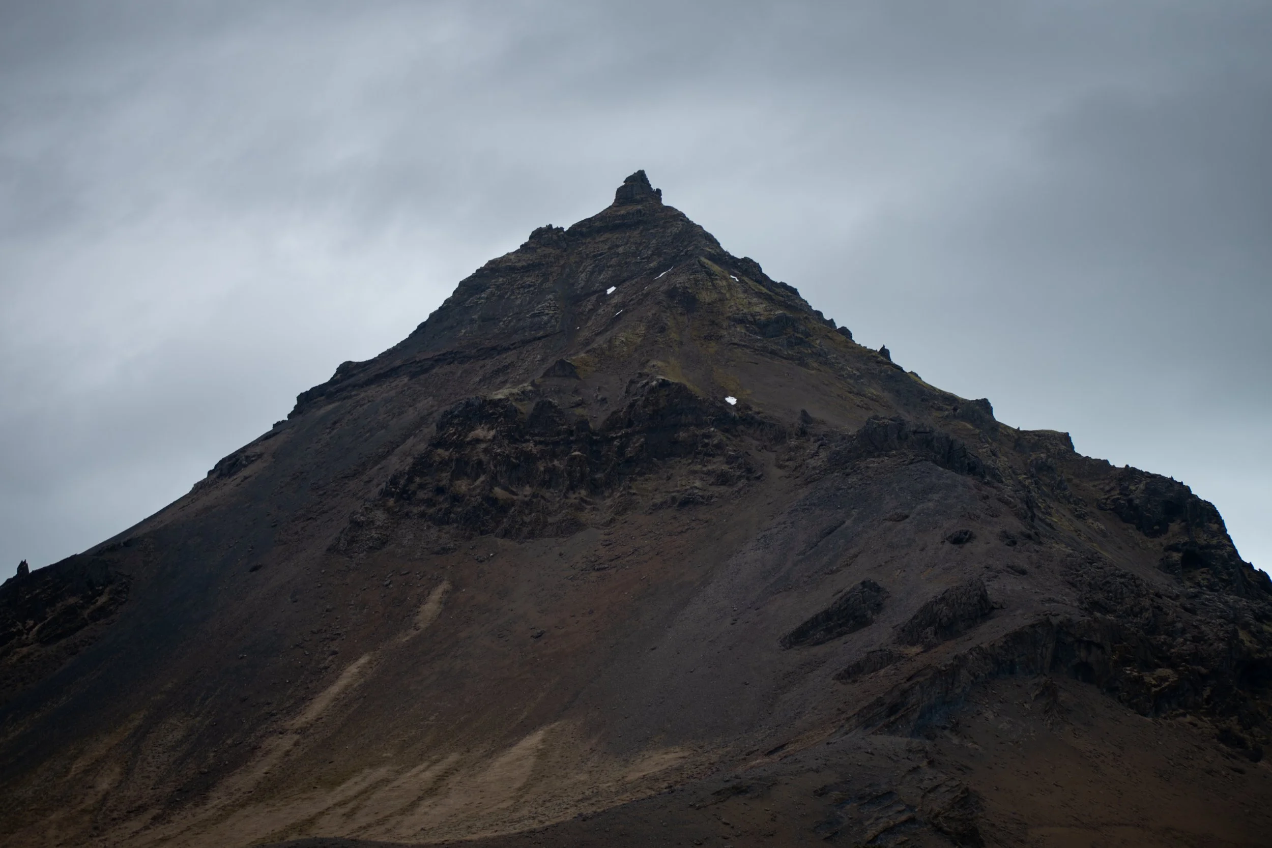 A rugged mountain peak with dark, rocky slopes under a cloudy sky.