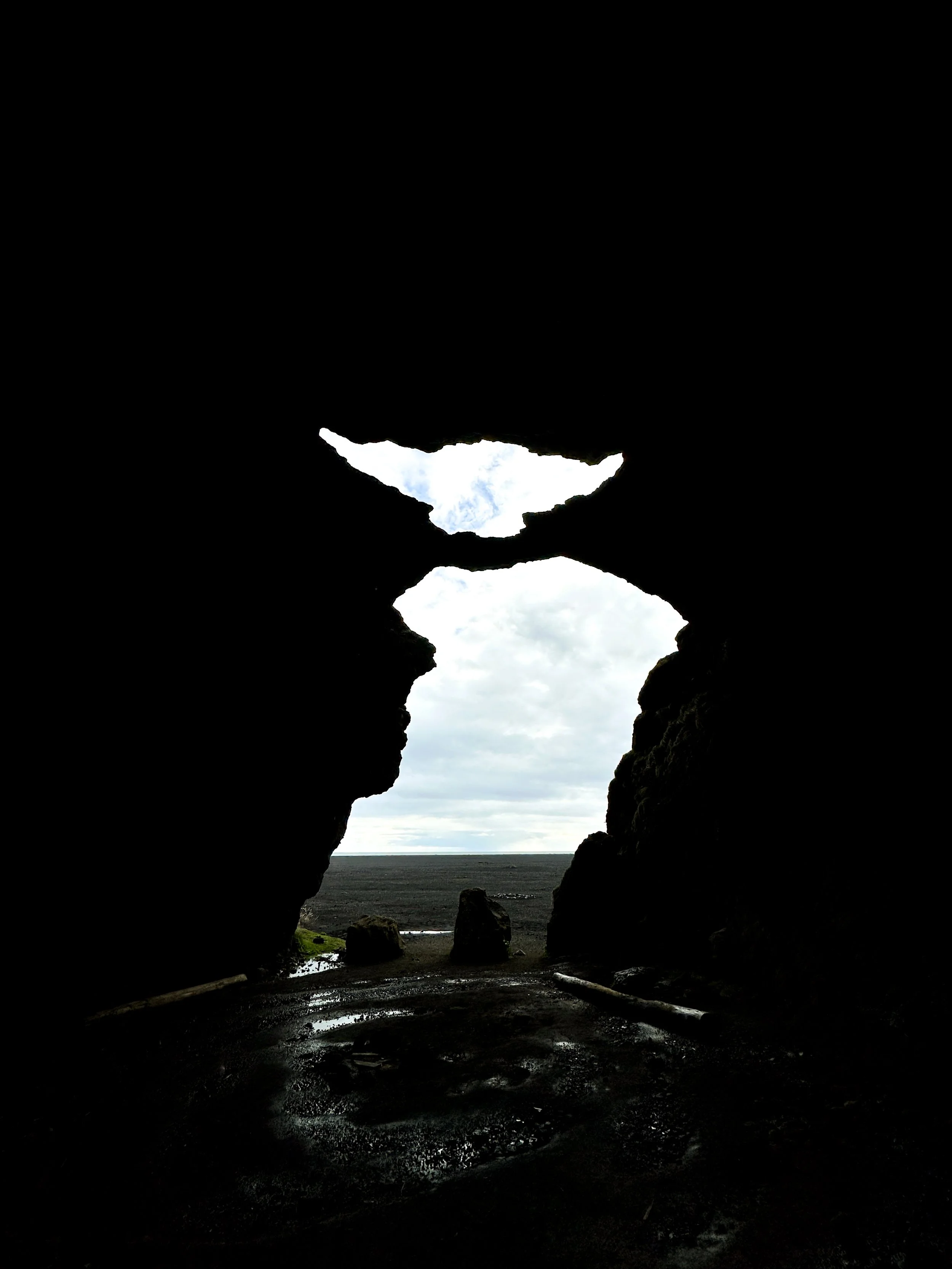 View through a rocky cave opening showing a cloudy sky, ocean, and landscape outside.