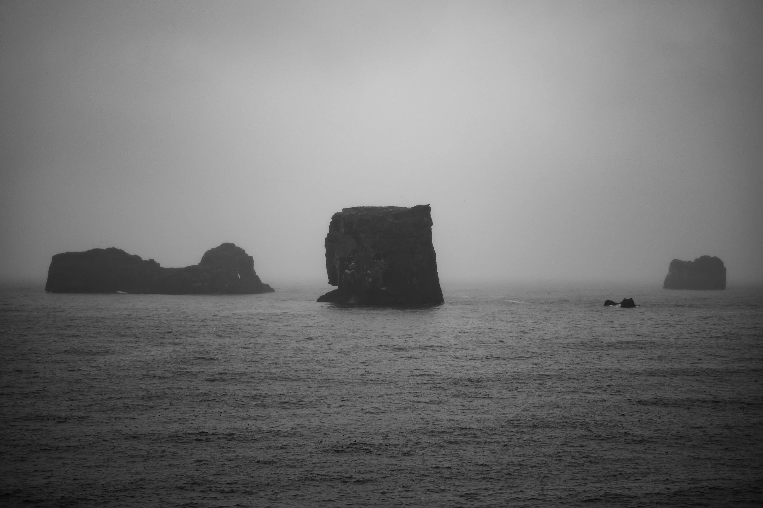 Black and white photograph of rocky sea stacks rising from ocean water, under an overcast sky.