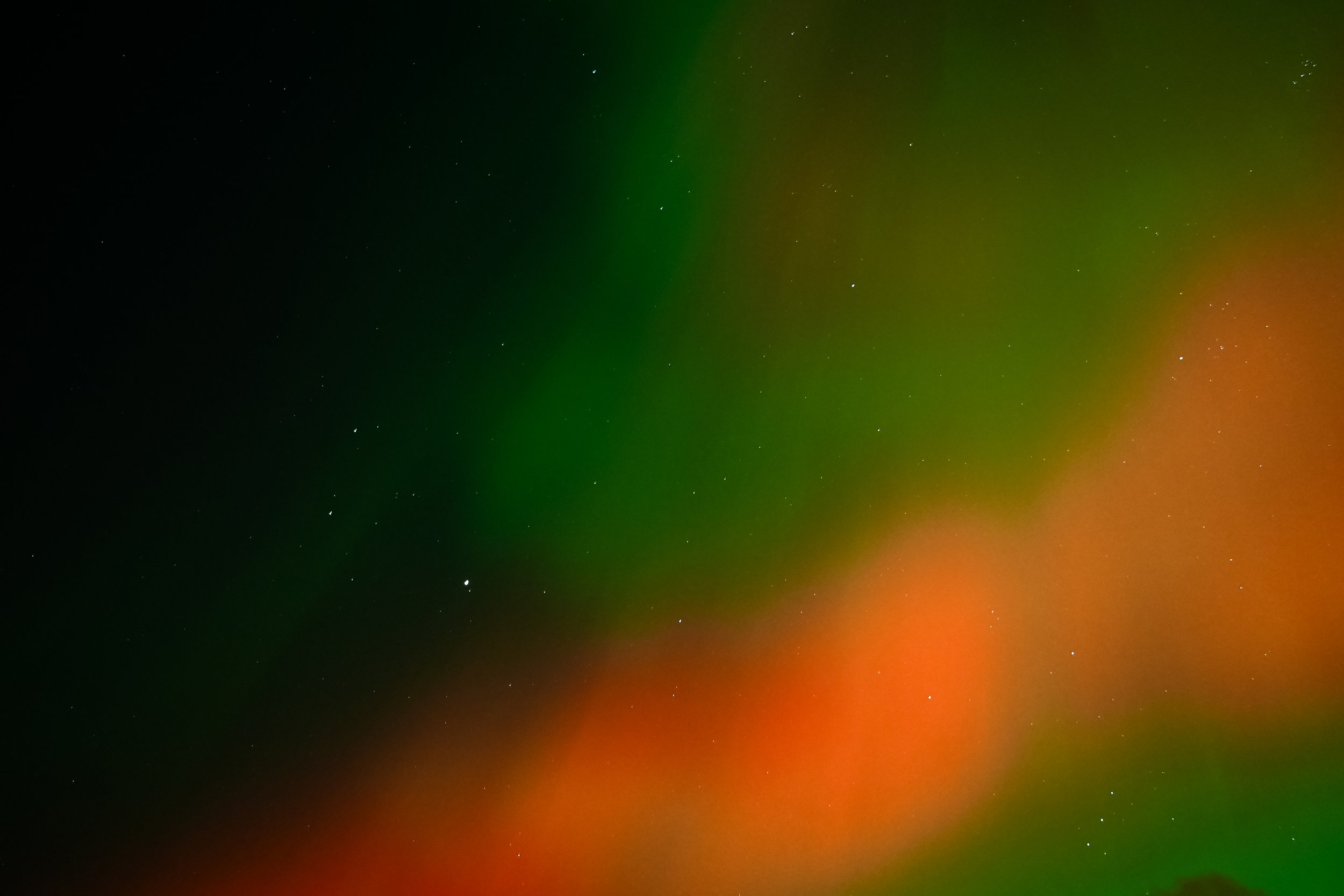 Photo of the night sky with visible stars and colorful aurora borealis in green and red hues.
