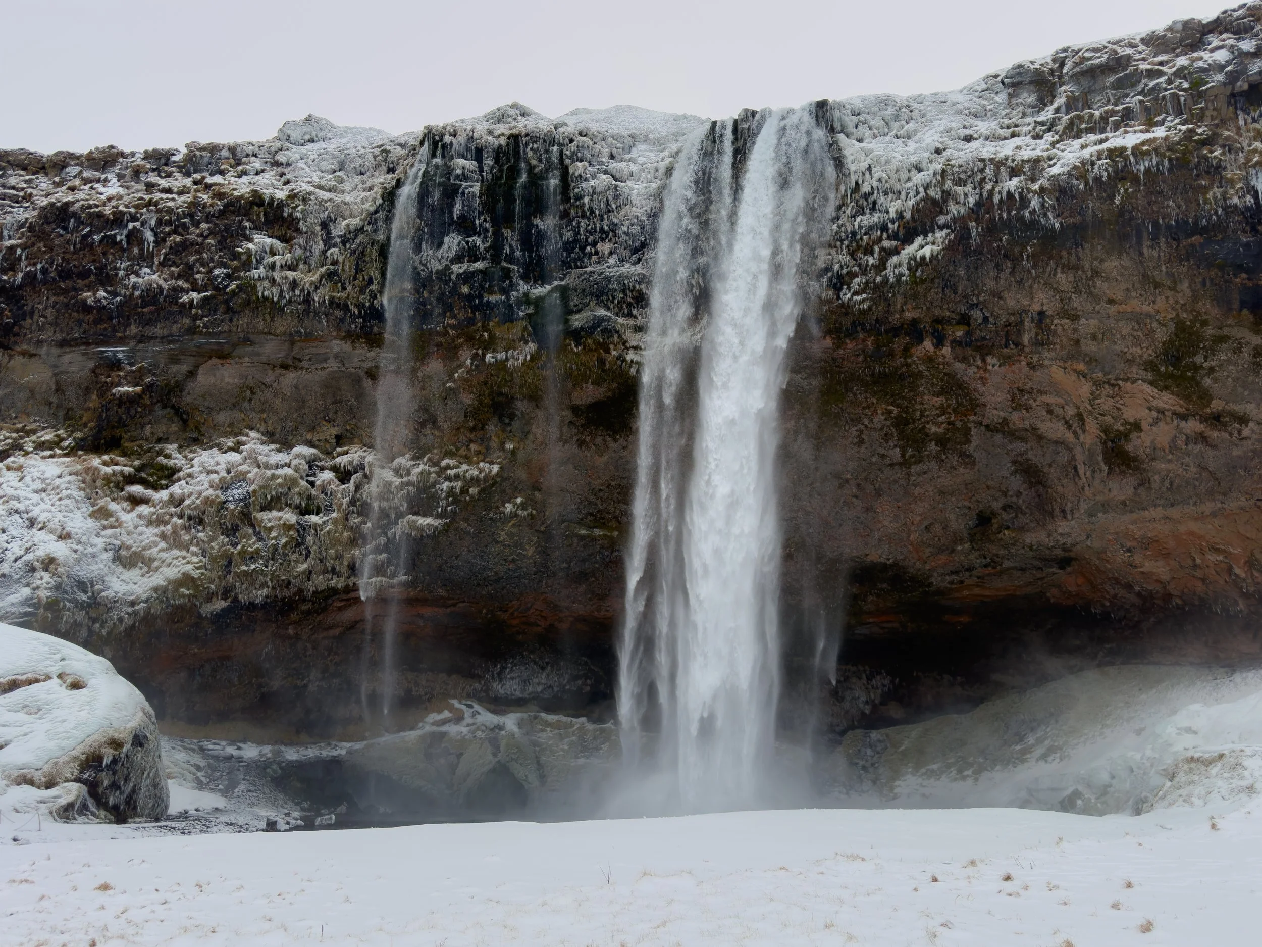 Waterfall in a snowy landscape with ice and snow-covered rocks.