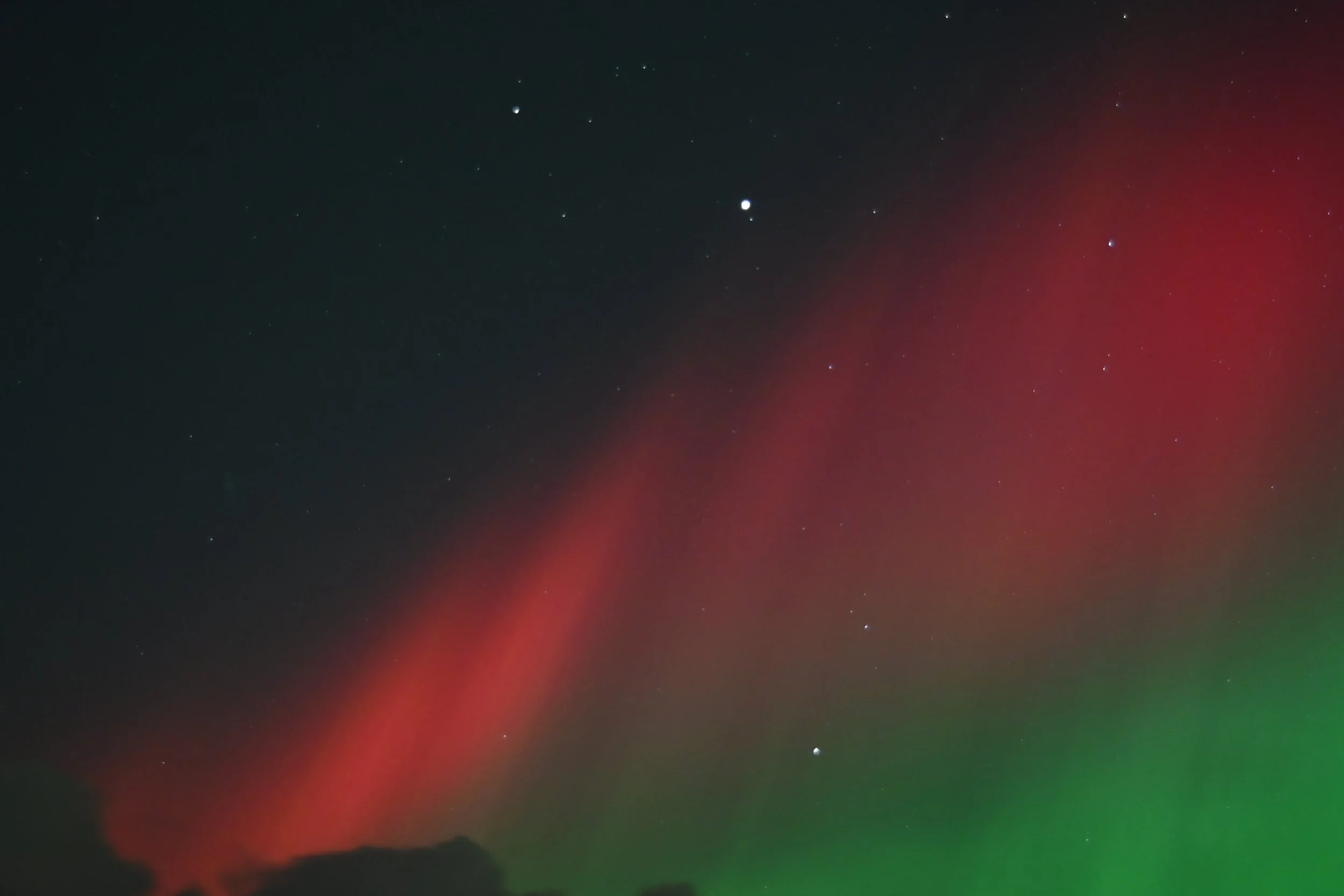 Night sky with stars and visible aurora borealis with red and green hues.