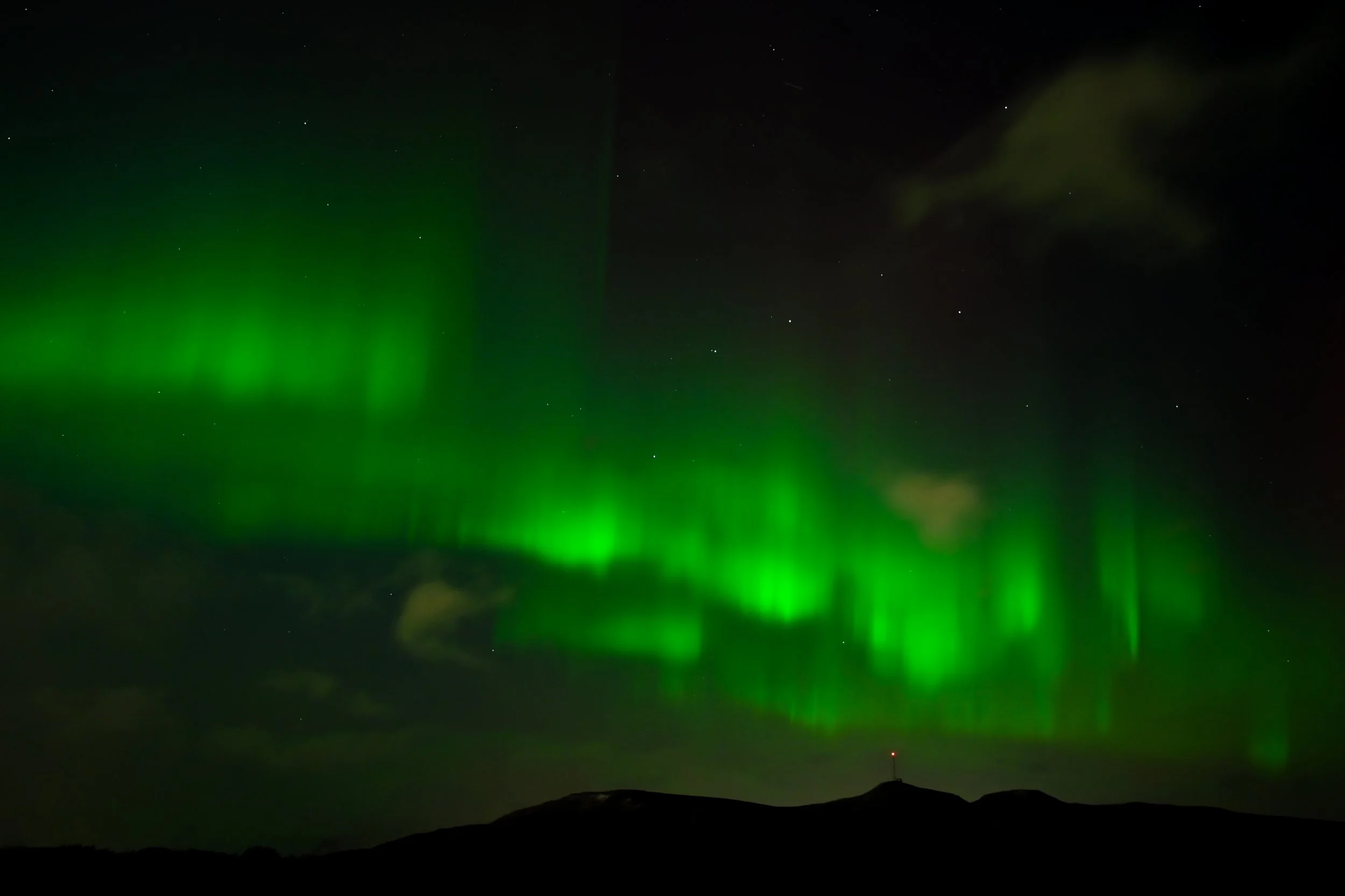 Night sky with green Northern Lights over dark mountain landscape.