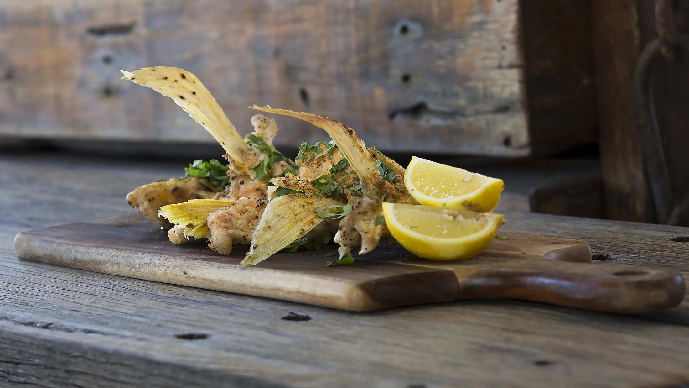 Fried fish with lemon wedges and fresh herbs on a wooden cutting board.