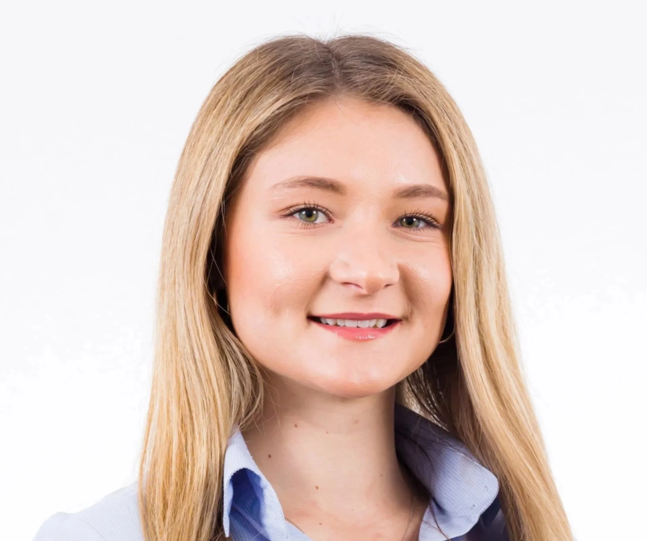 Close-up of a young woman with long blond hair, light makeup, and a light blue collared shirt smiling against a white background.