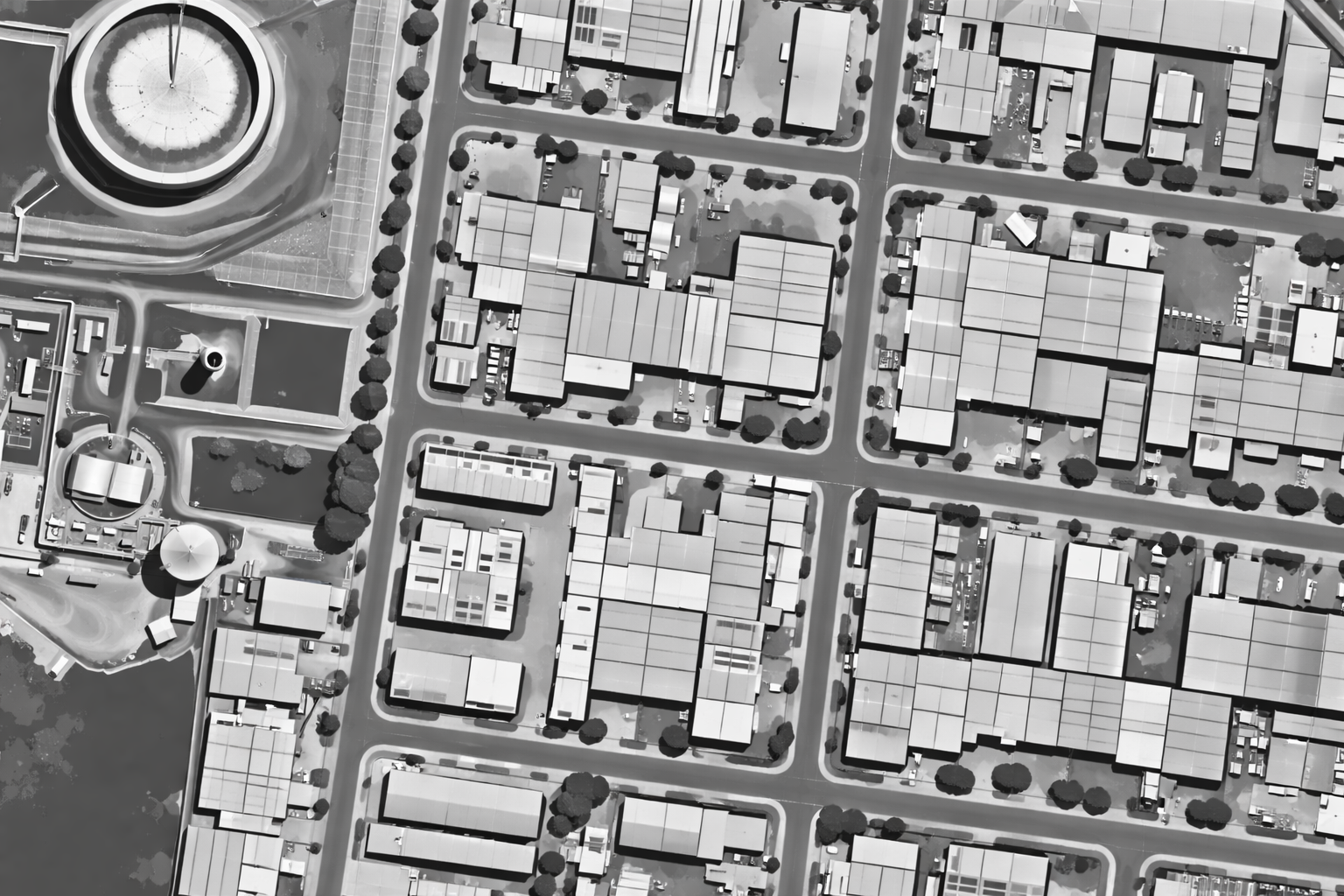 An aerial view of a city block in black and white, showing streets, buildings, trees, and some open spaces.