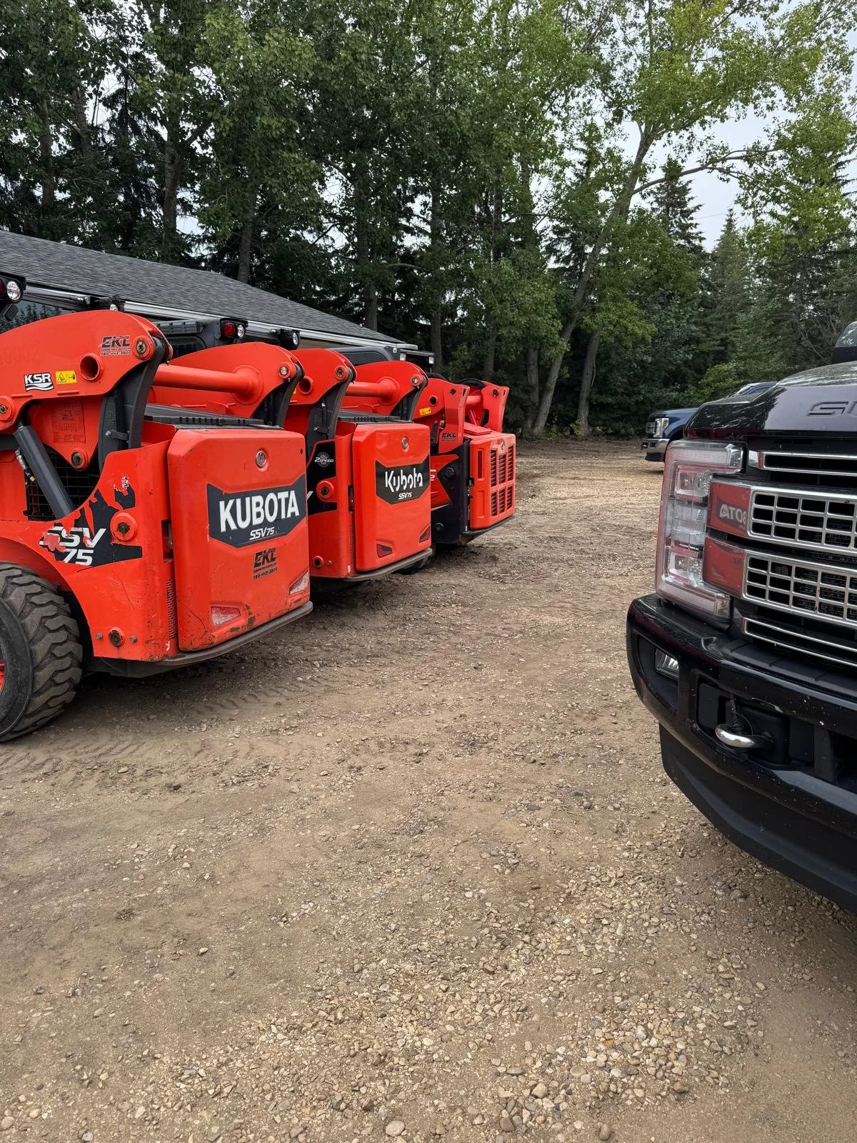 Red Kubota generators and equipment parked on a dirt lot with trees and vehicles in the background.