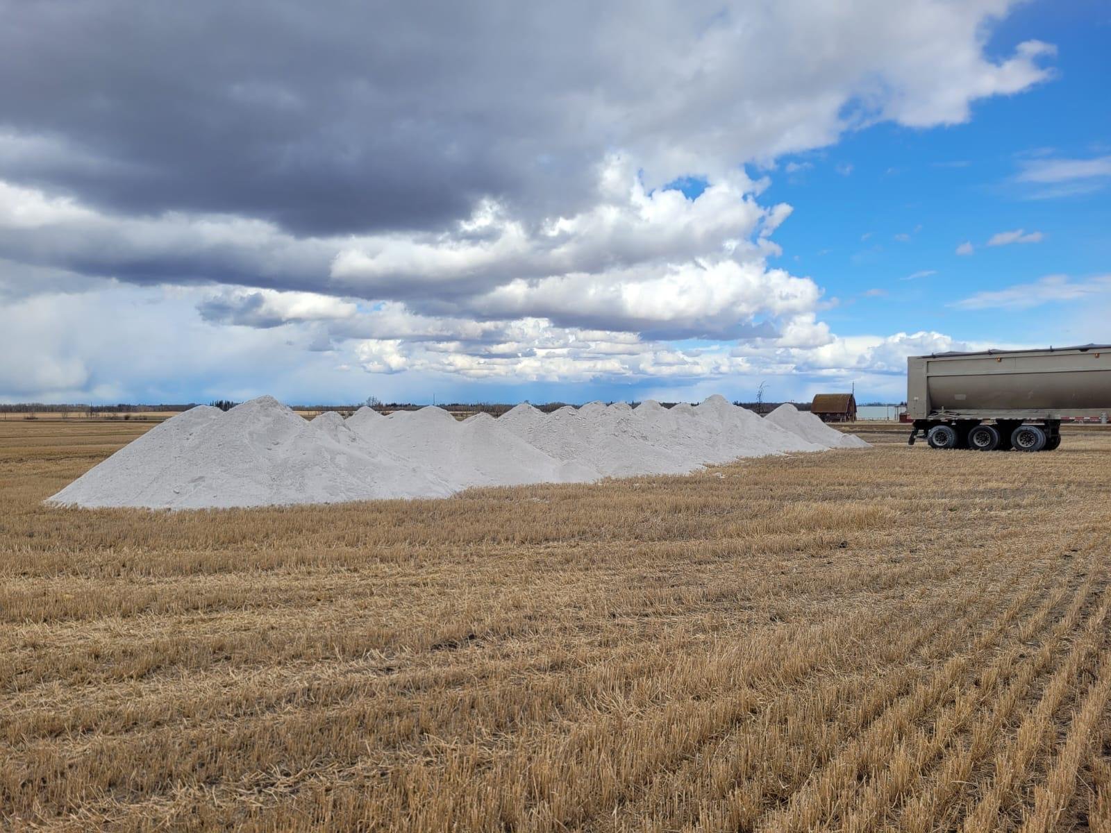 Large piles of salt in a field with a truck nearby under a partly cloudy sky.
