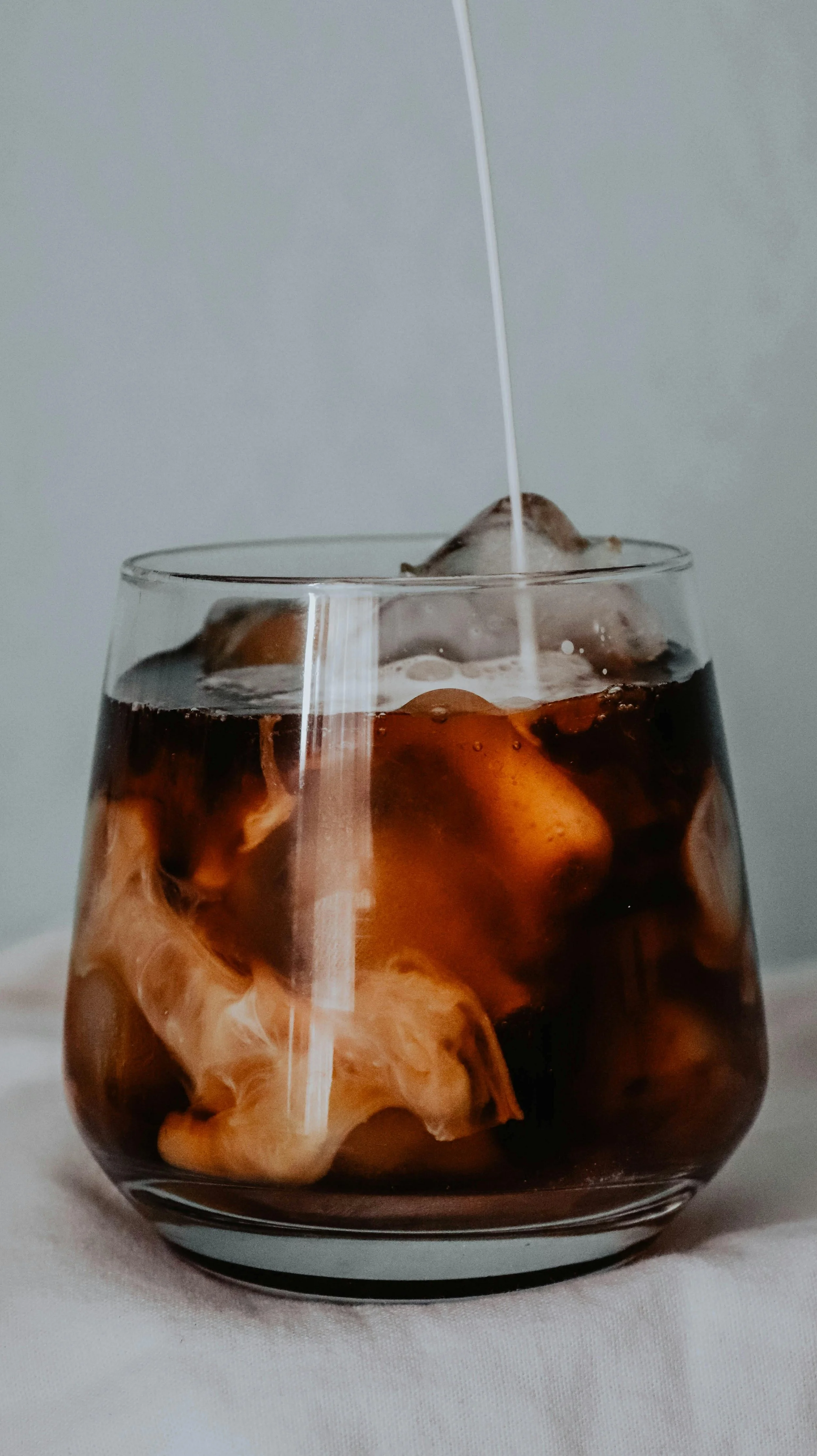 A glass of cold brew with ice cubes and milk being poured into it.