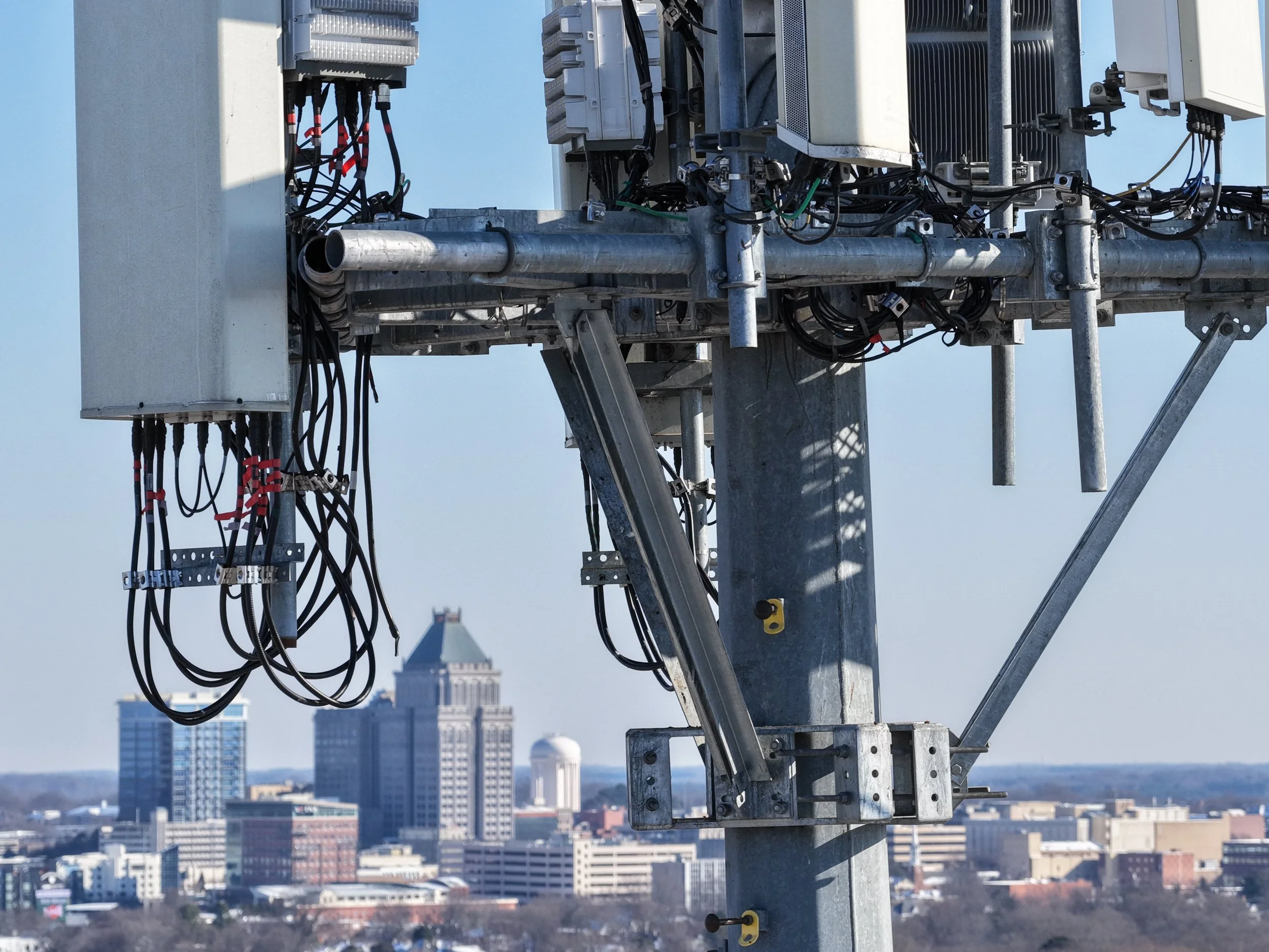Close-up of a cell tower antenna with a city skyline in the background.