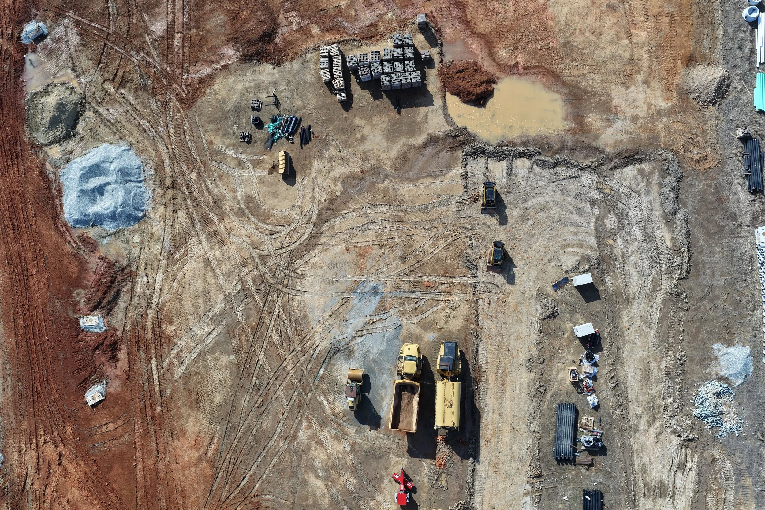 An aerial view of a construction site with machinery, construction materials, and dirt paths.