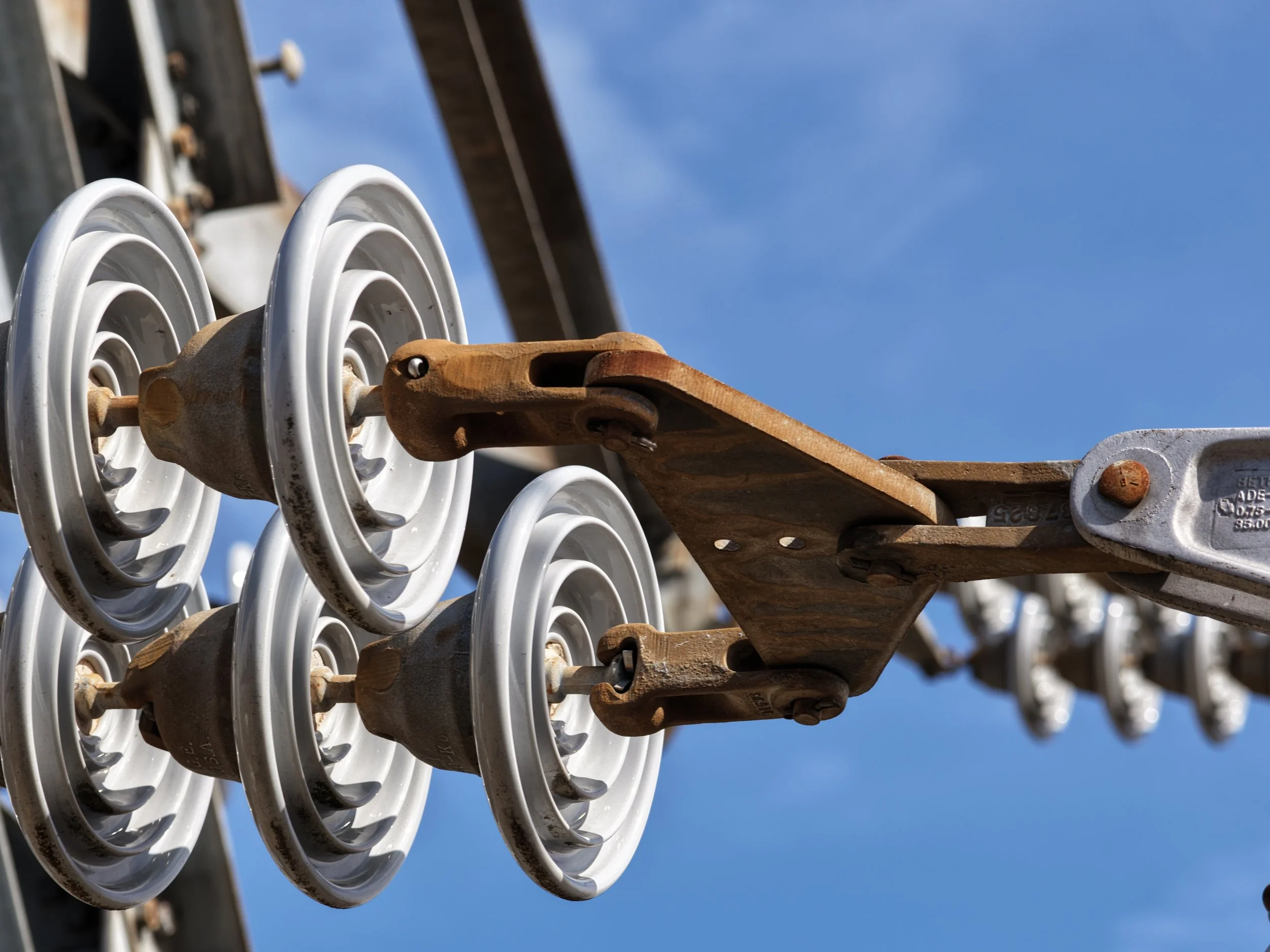 Close-up of electrical insulators mounted on a high-voltage power line against a blue sky.