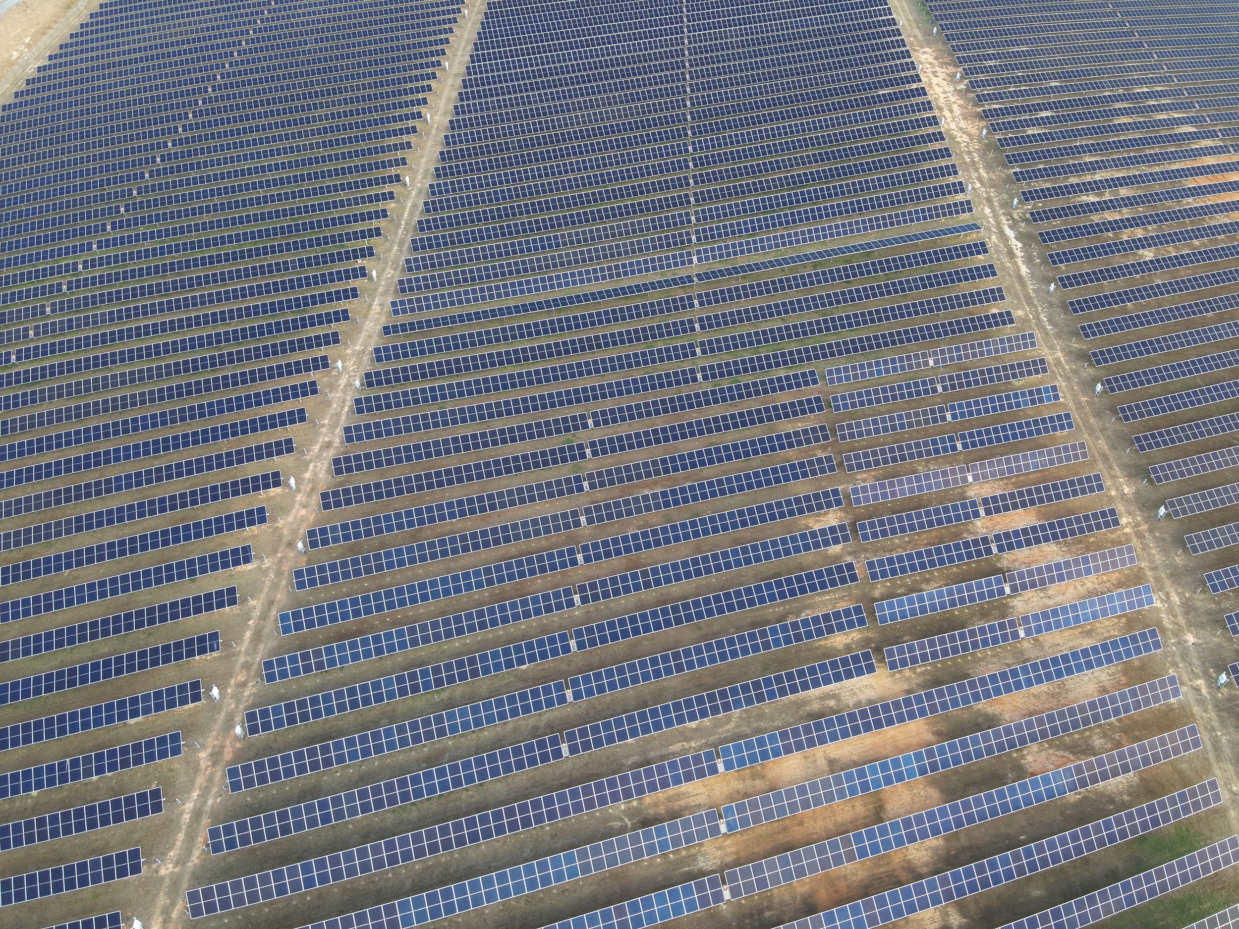 An aerial view of a large solar farm with numerous rows of solar panels installed on the ground.