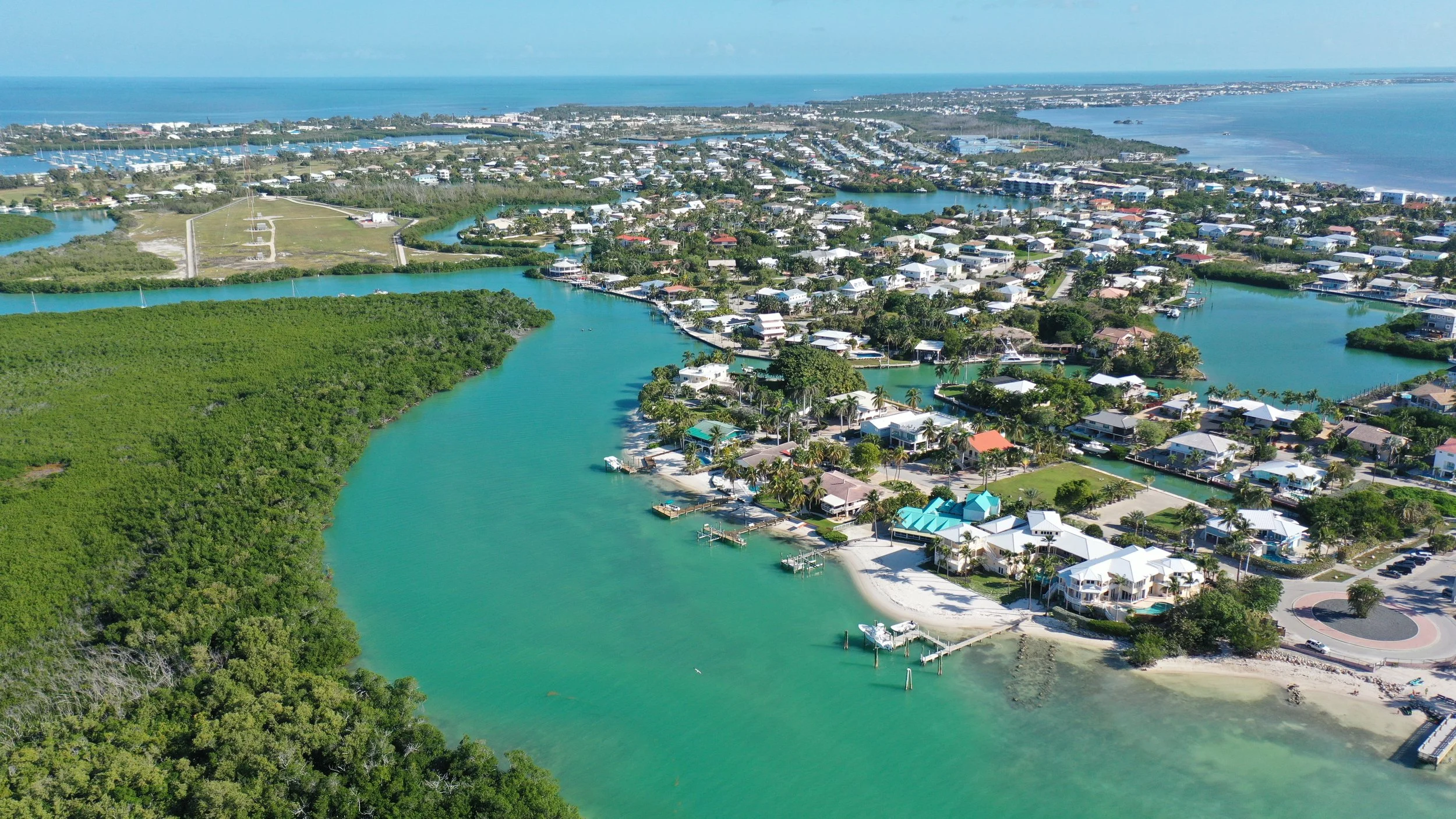 Aerial view of a coastal residential area with waterways, boats, and beaches, with the ocean in the background.