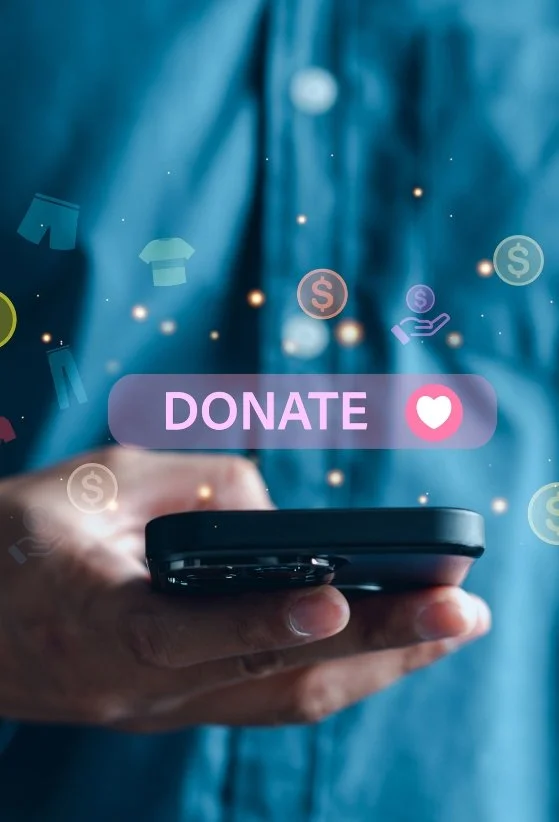 A person holding a smartphone with a donate button and heart icon on the screen, with digital icons of dollar signs and clothing in the background.