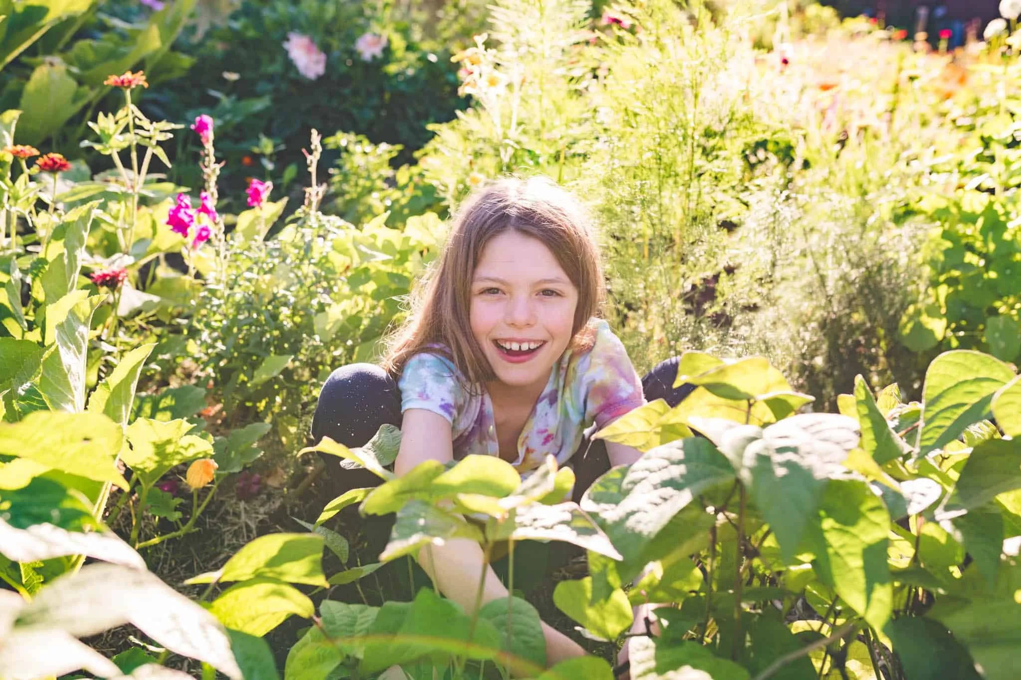 Girl smiling at camera while picking purple beans in a food forest garden.