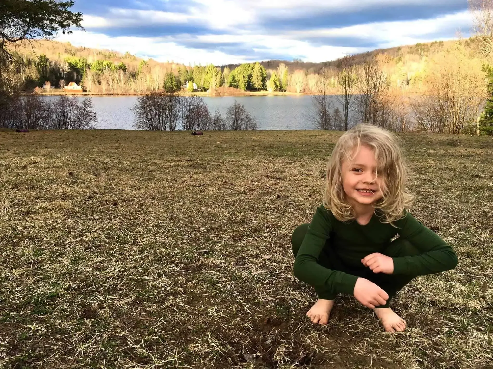 A small child standing on a grassy lawn in early spring when nothing is growing yet. This is a before photo of a future food forest.