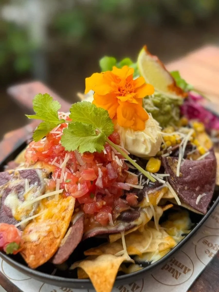 Close-up of nachos topped with diced tomatoes, shredded cheese, sour cream, fresh cilantro, a lime wedge, corn, beans, and shredded meat.