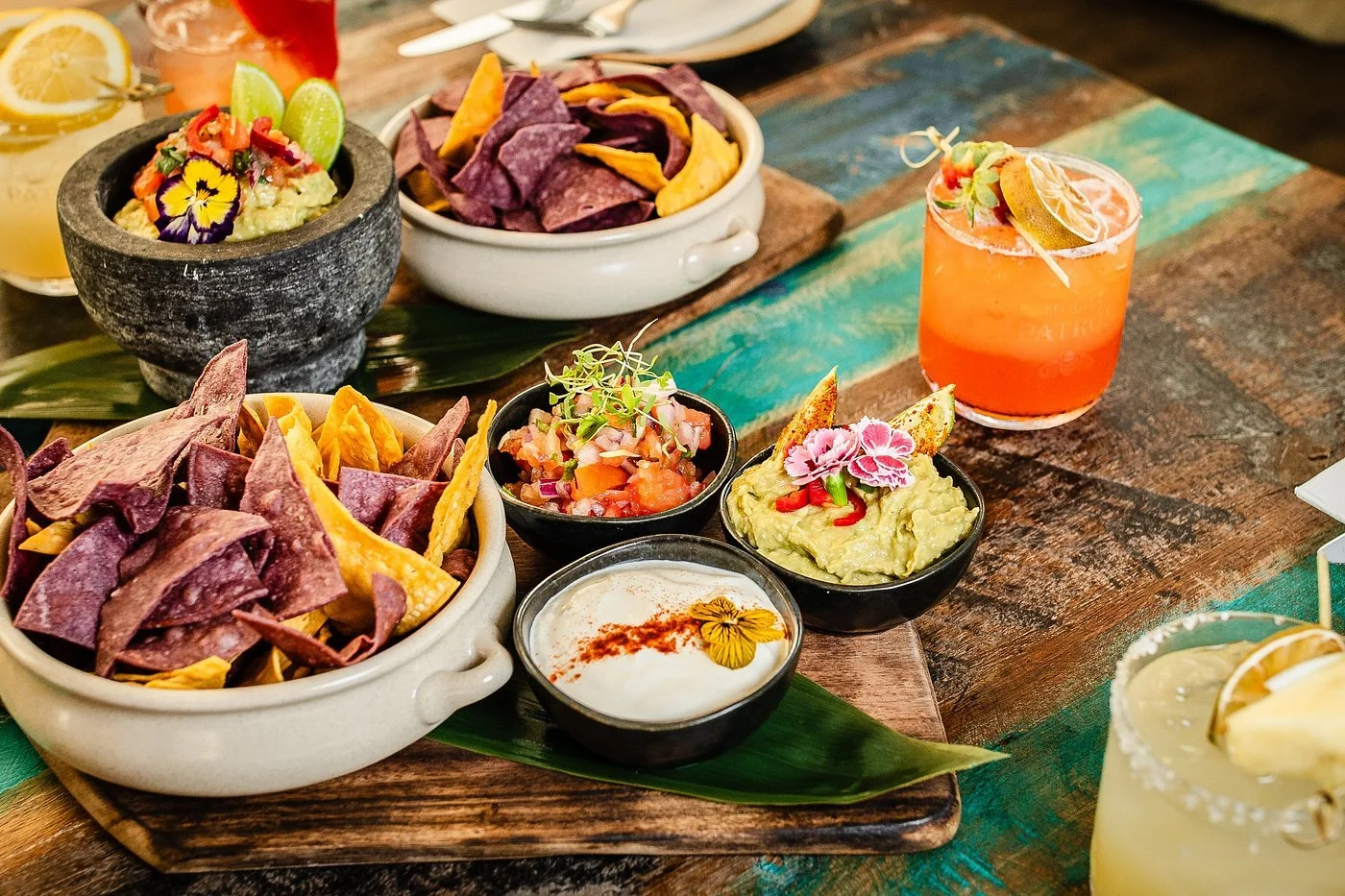 Mexican or Tex-Mex food with tortilla chips, guacamole, pico de gallo, and drinks on a wooden table.
