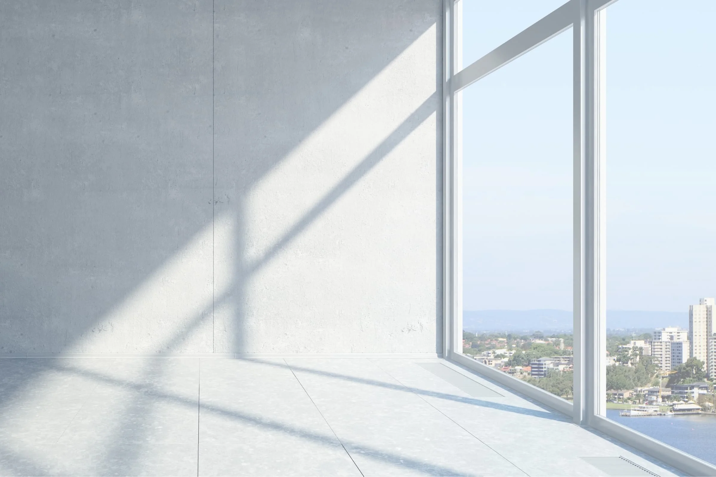 Empty modern interior room with large floor-to-ceiling windows showing a cityscape view, sunlight casting shadows on the light gray walls and floor.