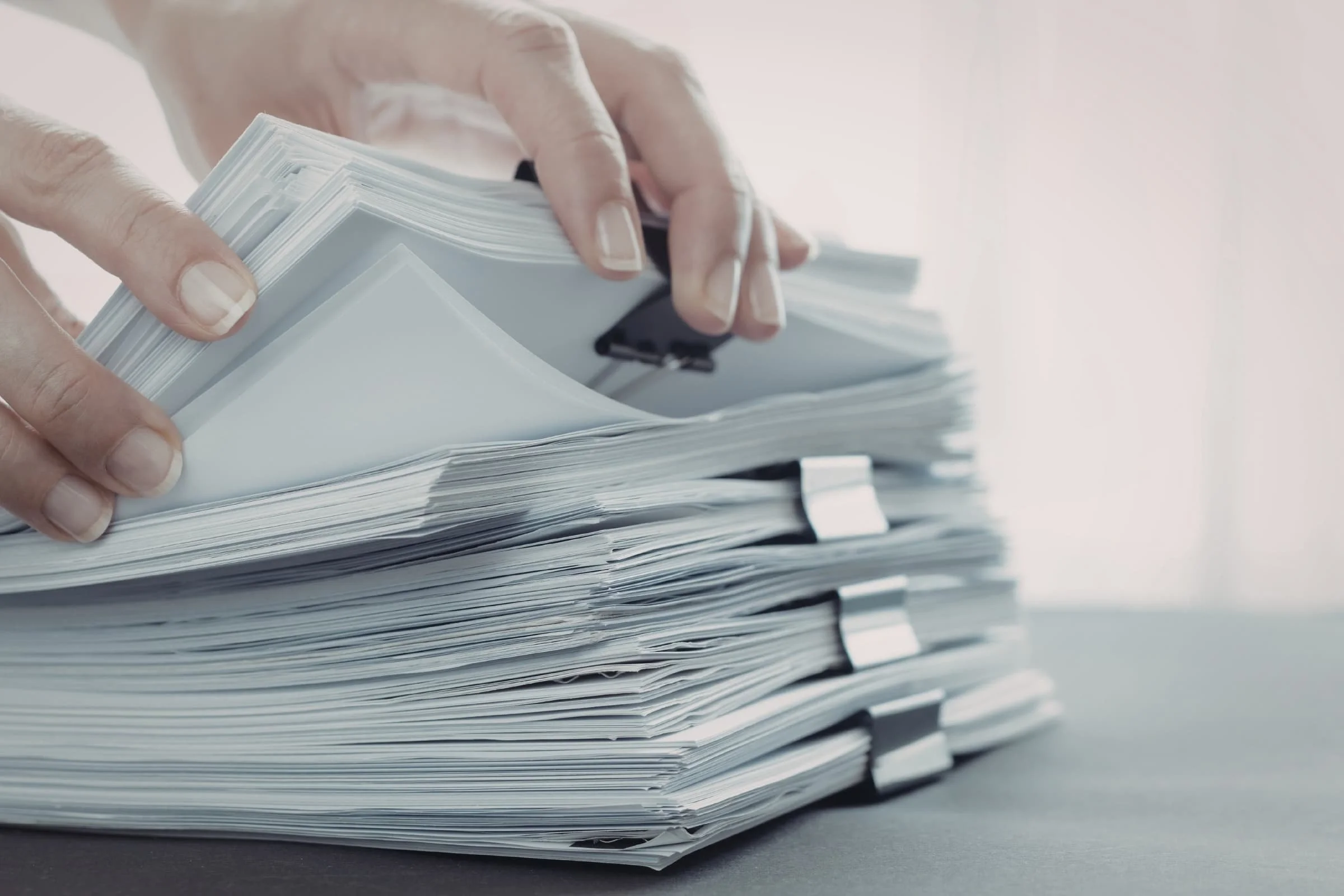 Close-up of a hand flipping through a large stack of papers held together with a black clip.