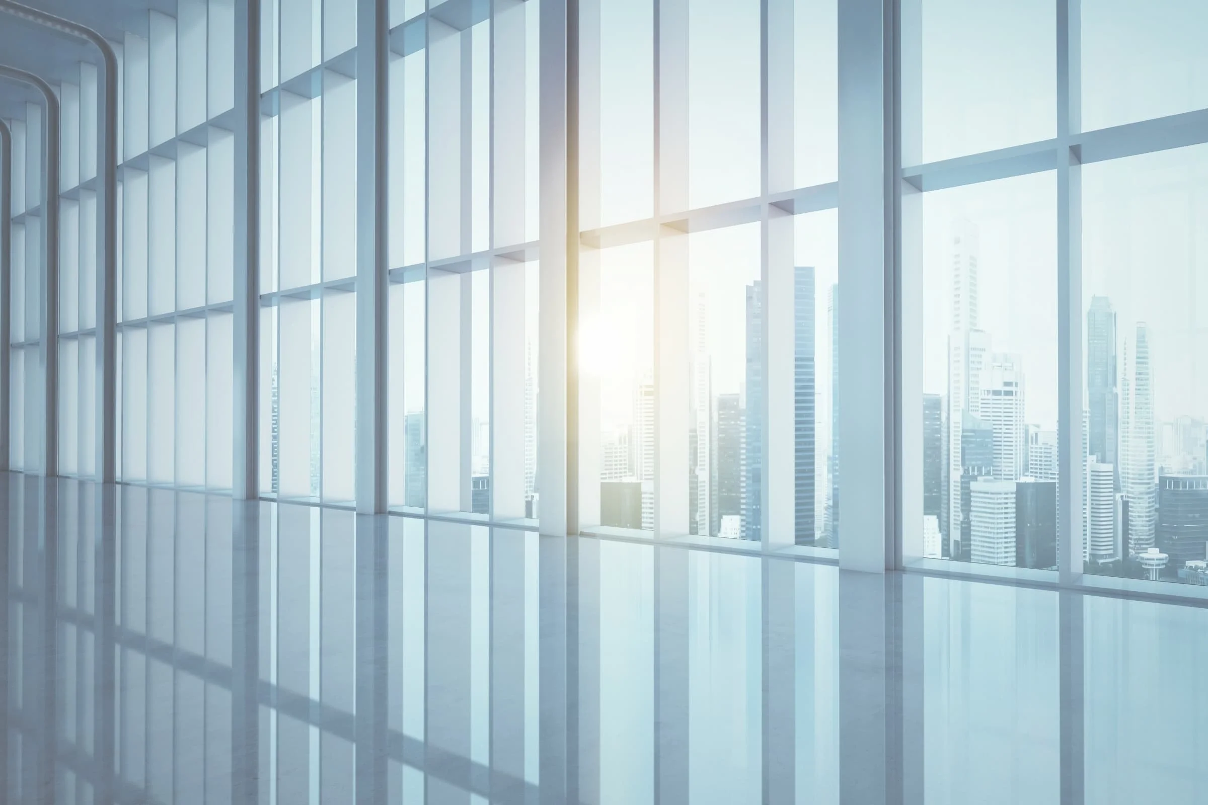 Sunlight coming through large glass windows in a modern high-rise building, overlooking a city skyline with tall buildings.