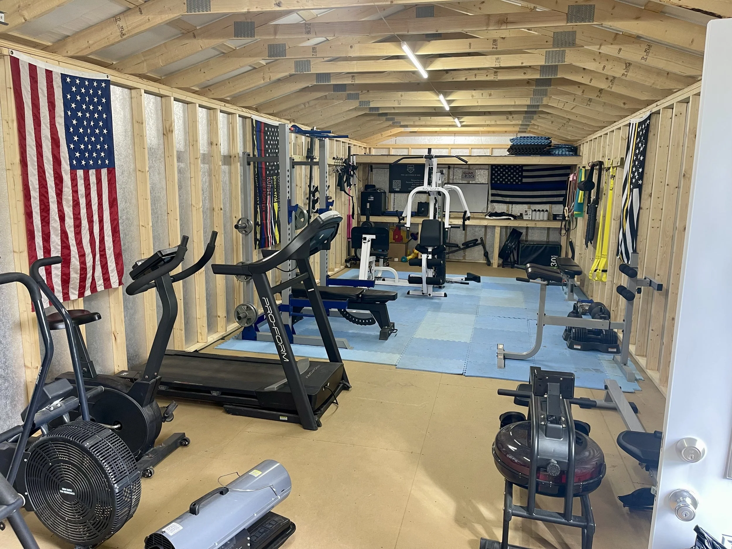 A home gym with various exercise equipment, American flags on the walls, and wooden walls and ceiling.