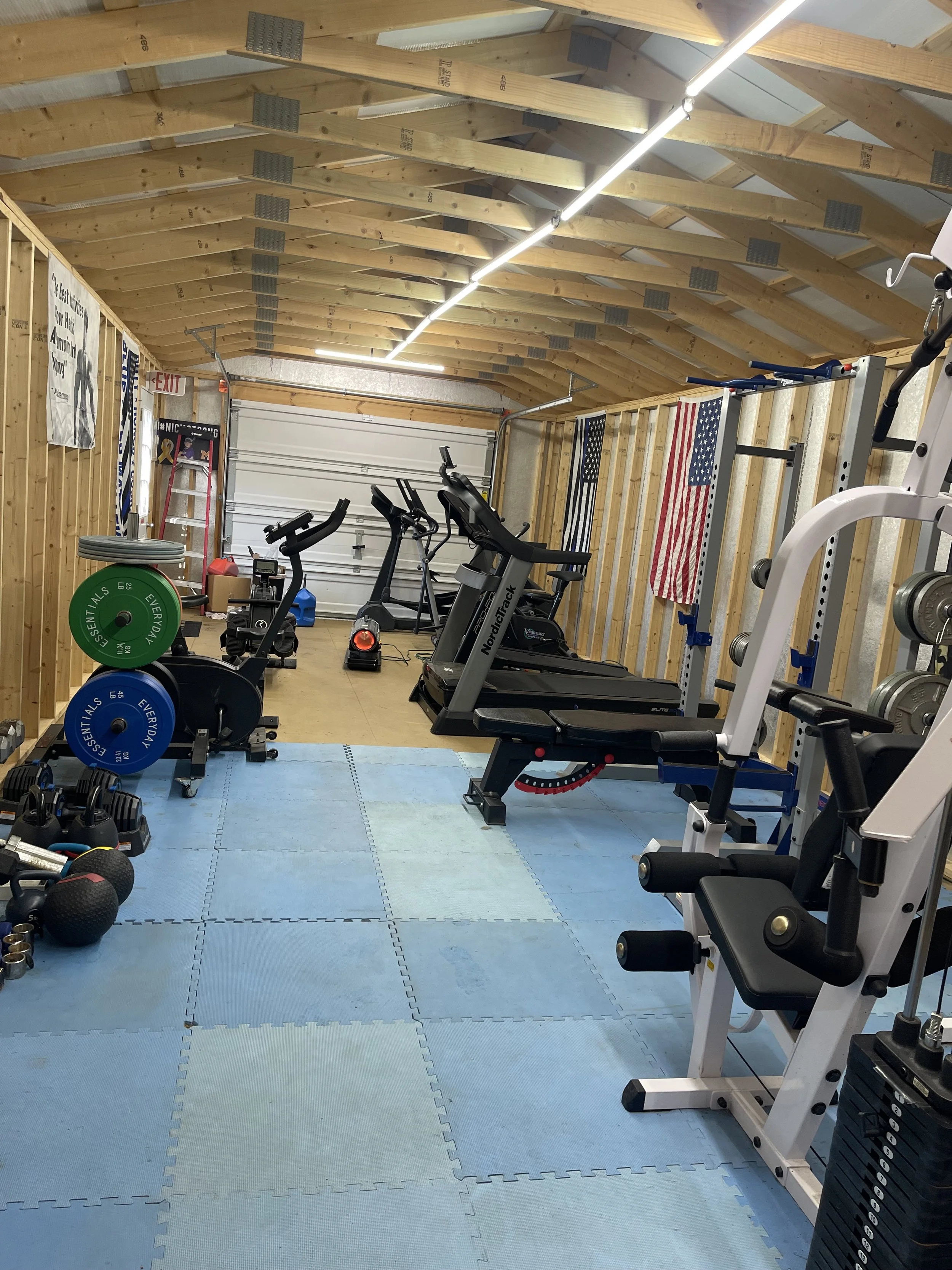 Home gym with treadmills, weights, and American flags on the wall in a wooden-finished garage.