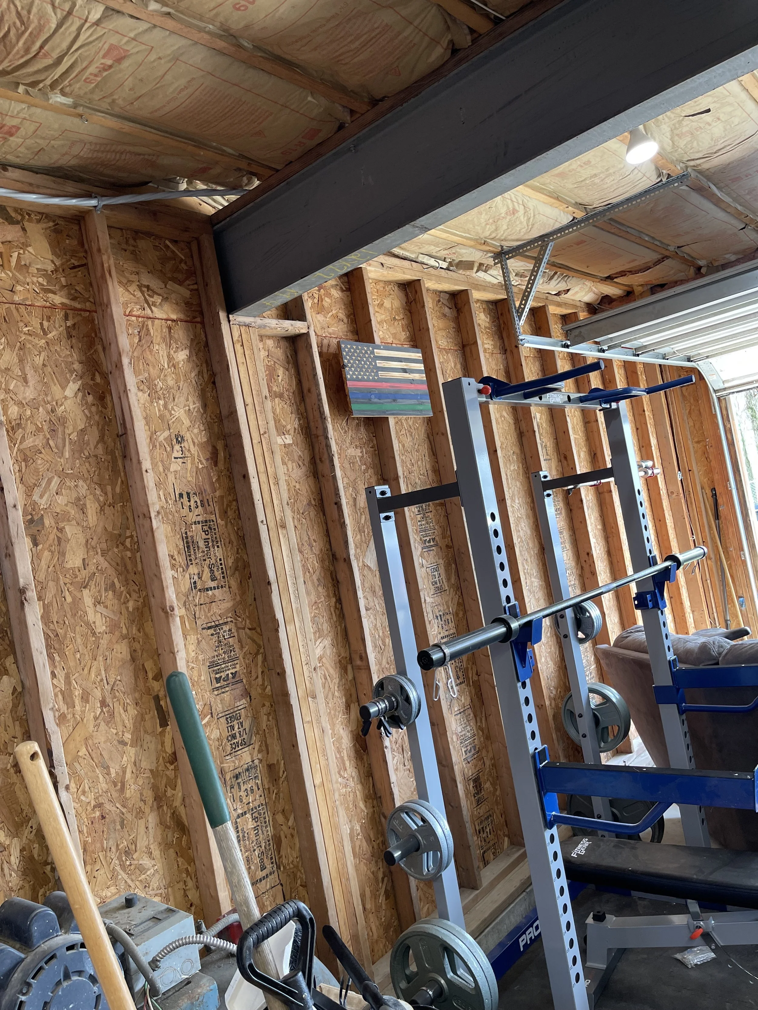 Inside a partially finished garage gym with wood framing, gym equipment, and a flag-shaped wall art.
